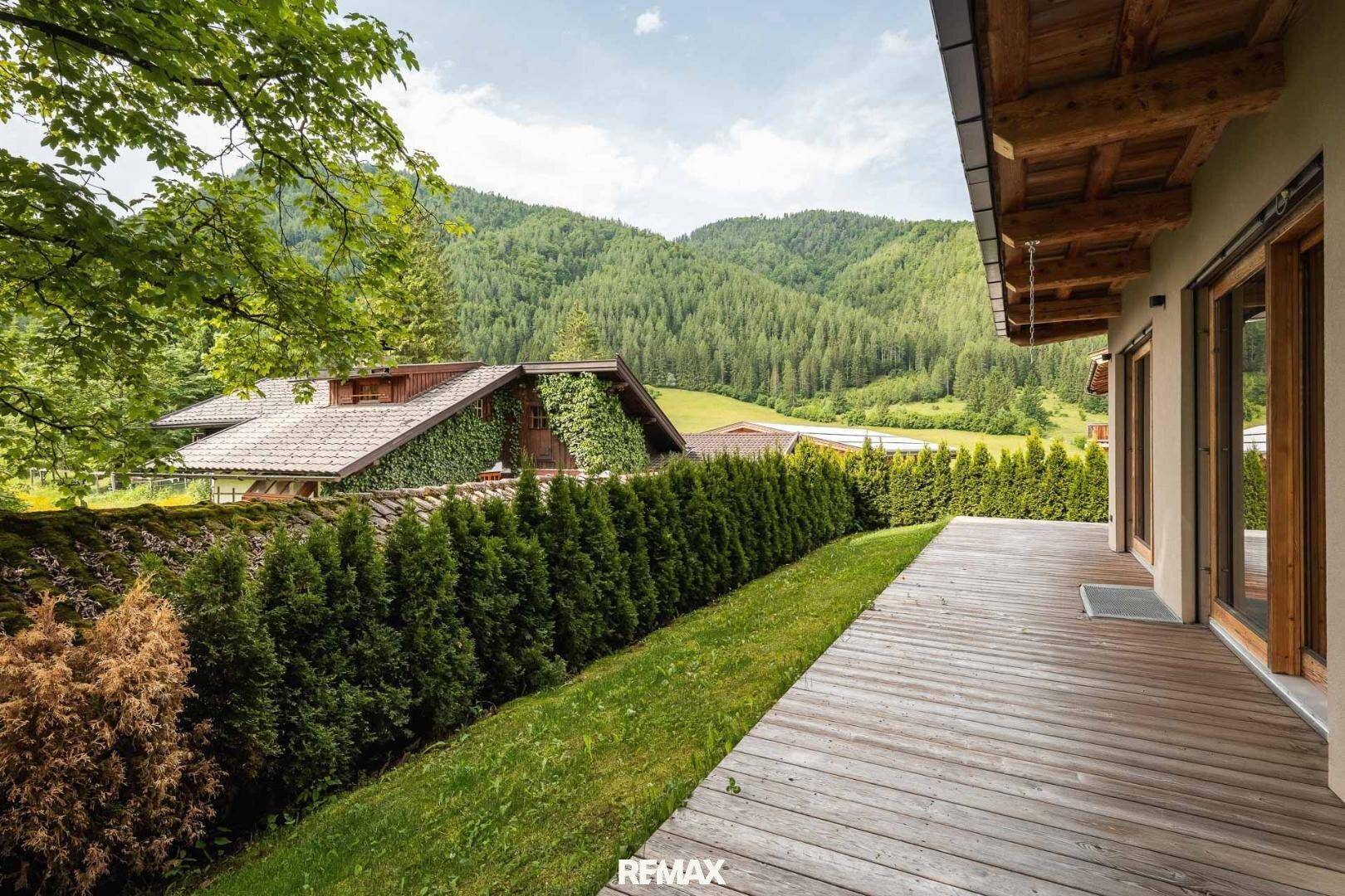 Holzterrasse mit Hecke und weitem Blick auf die umliegende Berglandschaft.
