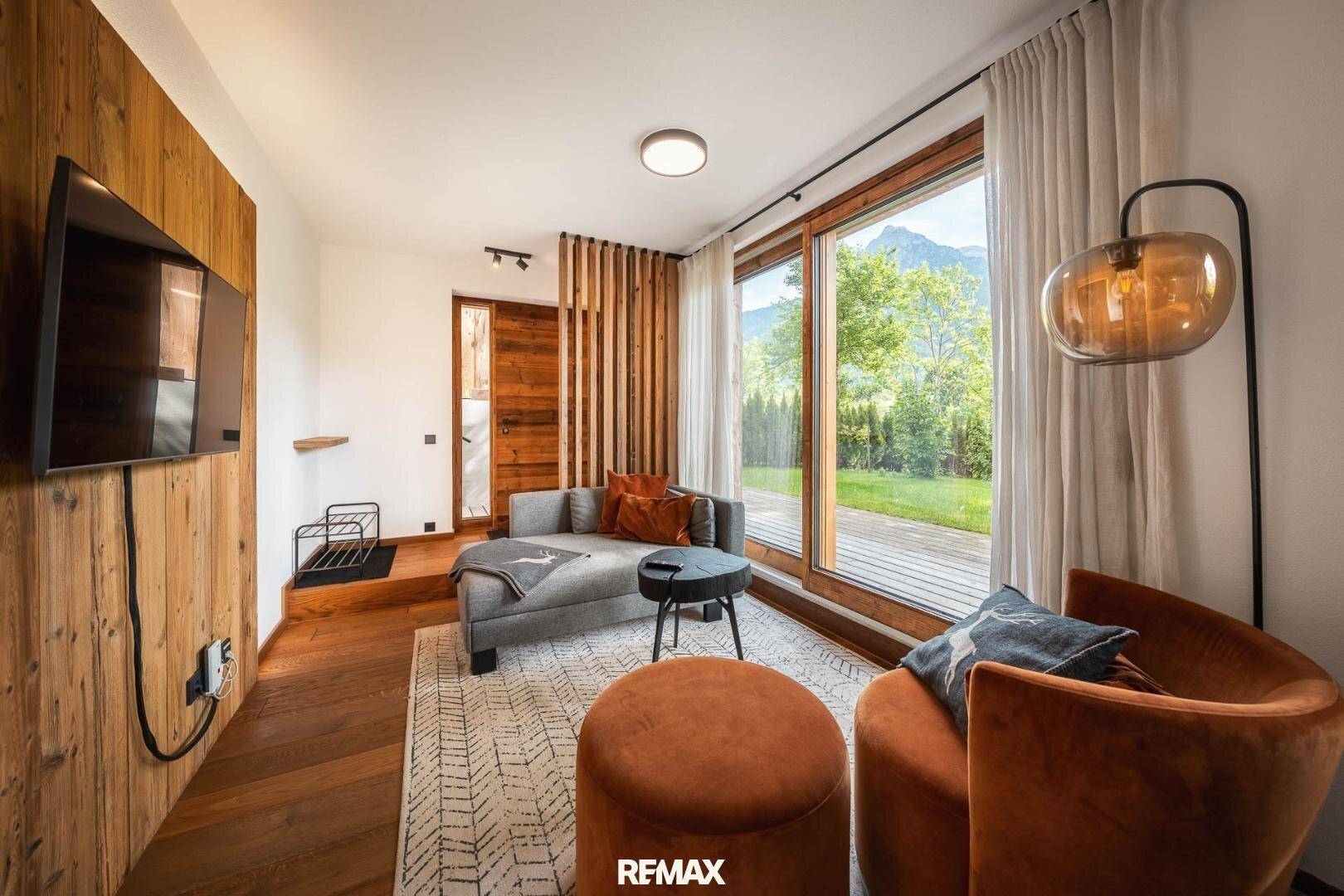Helles Wohnzimmer mit Holzboden, großem Fenster und Blick ins Grüne.