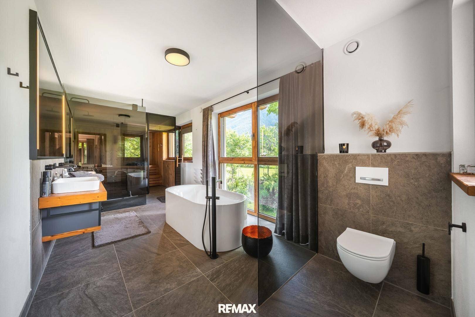 Modernes Badezimmer mit freistehender Badewanne, Doppelwaschbecken und großen Fenstern.