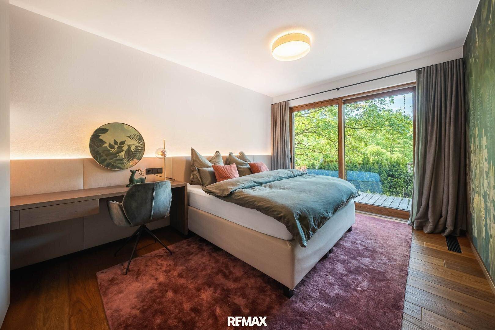 Gemütliches Schlafzimmer mit Holzboden, großem Fenster und Blick ins Grüne.