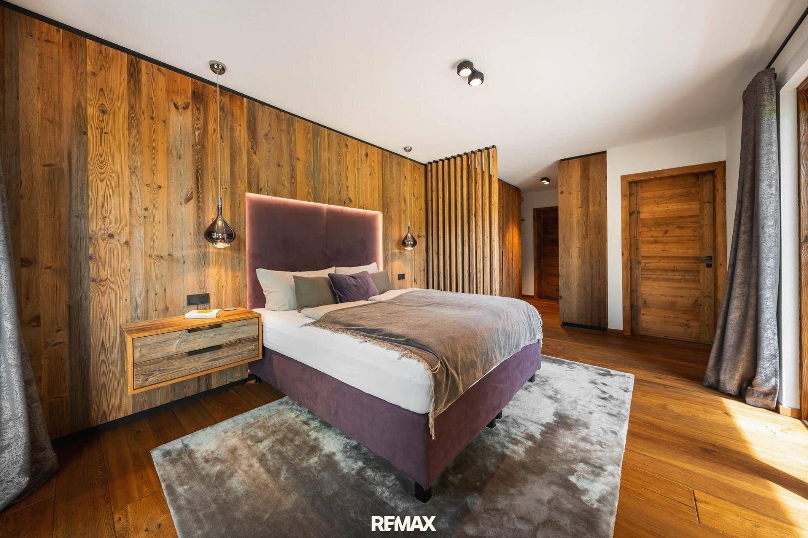 Modernes Schlafzimmer mit Holzwand, großem Bett und weichem Teppichboden.