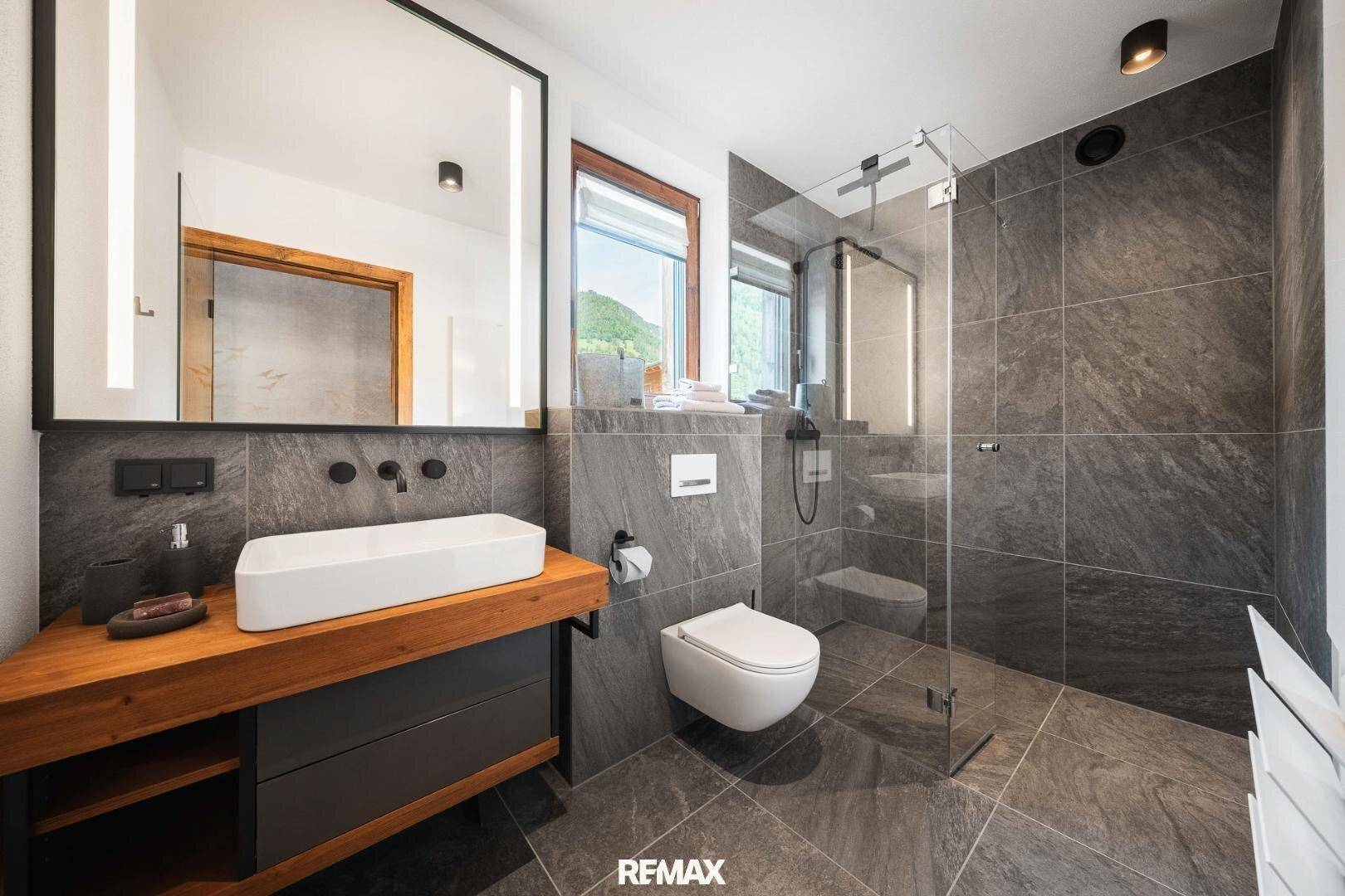 Modernes Badezimmer mit großem Spiegel, Einzelwaschbecken und begehbarer Dusche.