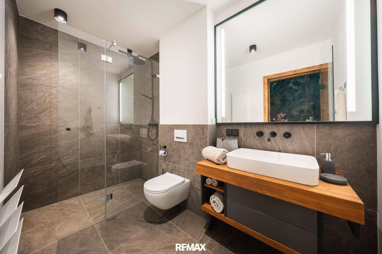 Modernes Badezimmer mit großem Spiegel, Einzelwaschbecken und begehbarer Dusche.