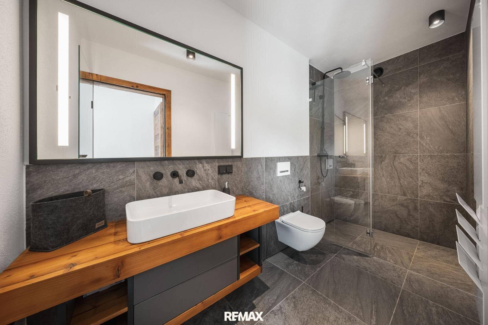 Modernes Badezimmer mit großem Spiegel, Einzelwaschbecken und begehbarer Dusche.