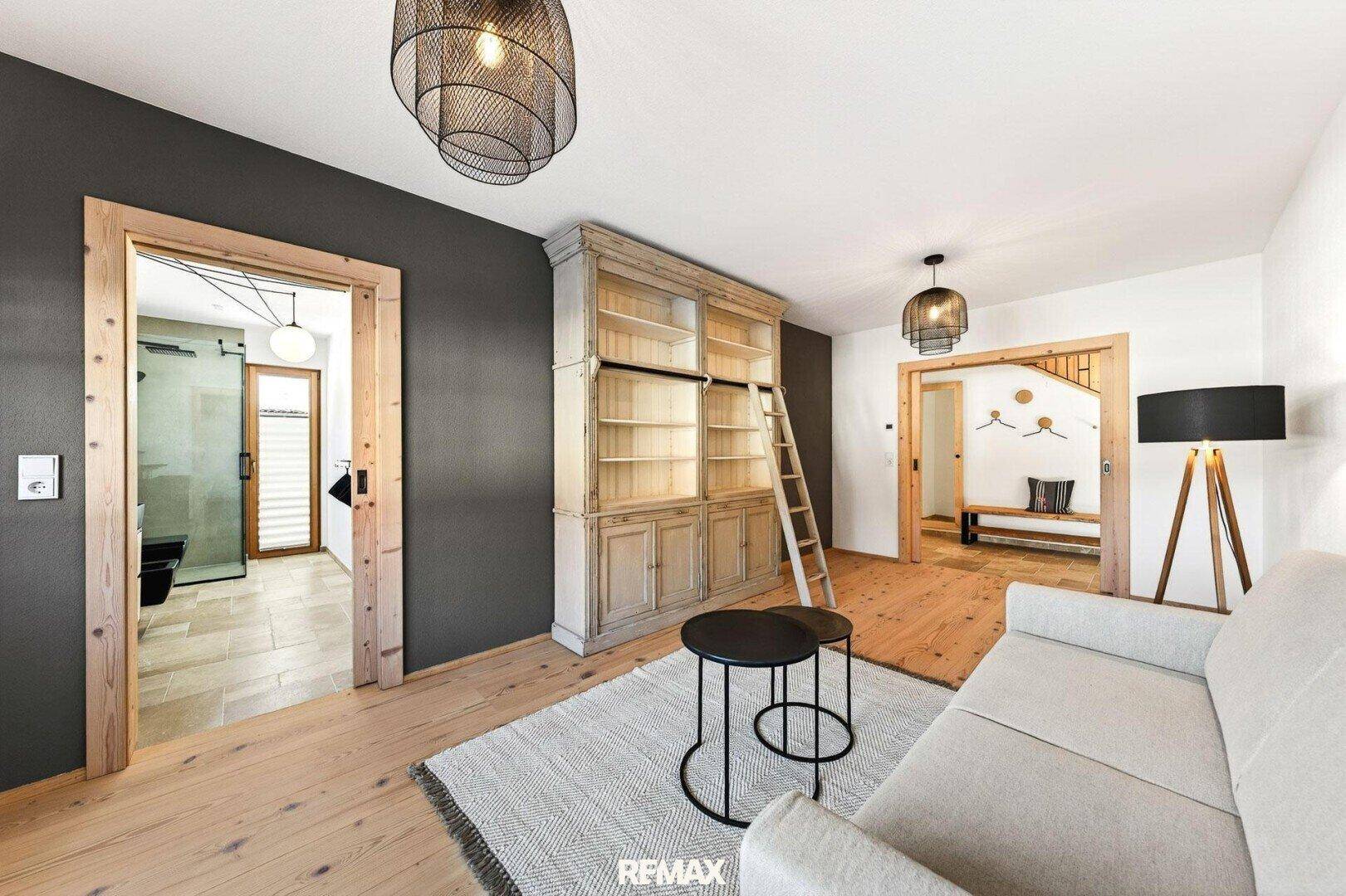 Gemütliches Wohnzimmer mit Sofa, Teppich, Bücherregal und Zugang zu weiteren Räumen.