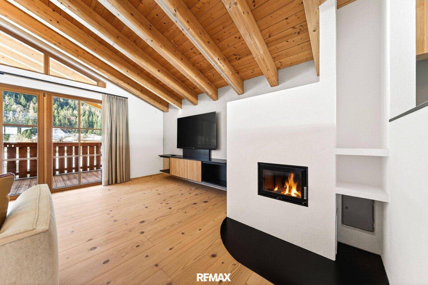 Moderner Wohnbereich mit integriertem Kamin, Fernseher und Zugang zu einem Balkon.