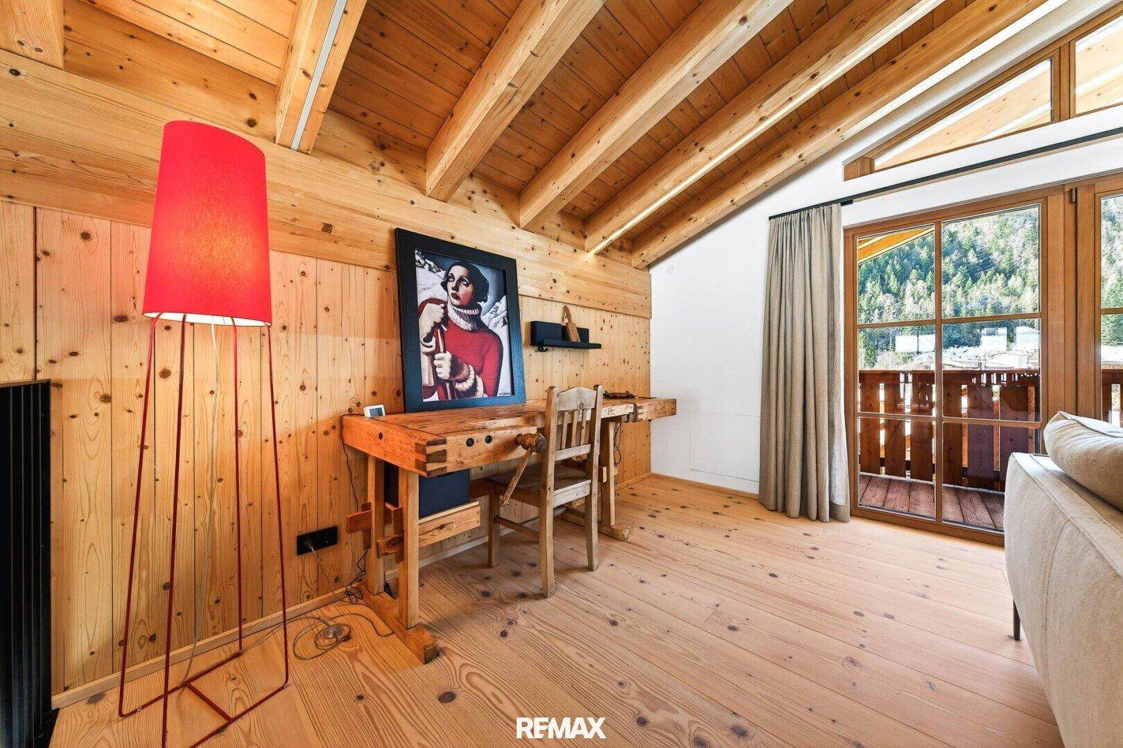 Gemütlicher Raum mit Holzbalkendecke, Holzboden und Zugang zu einem Balkon, ideal als Büro oder Leseecke.