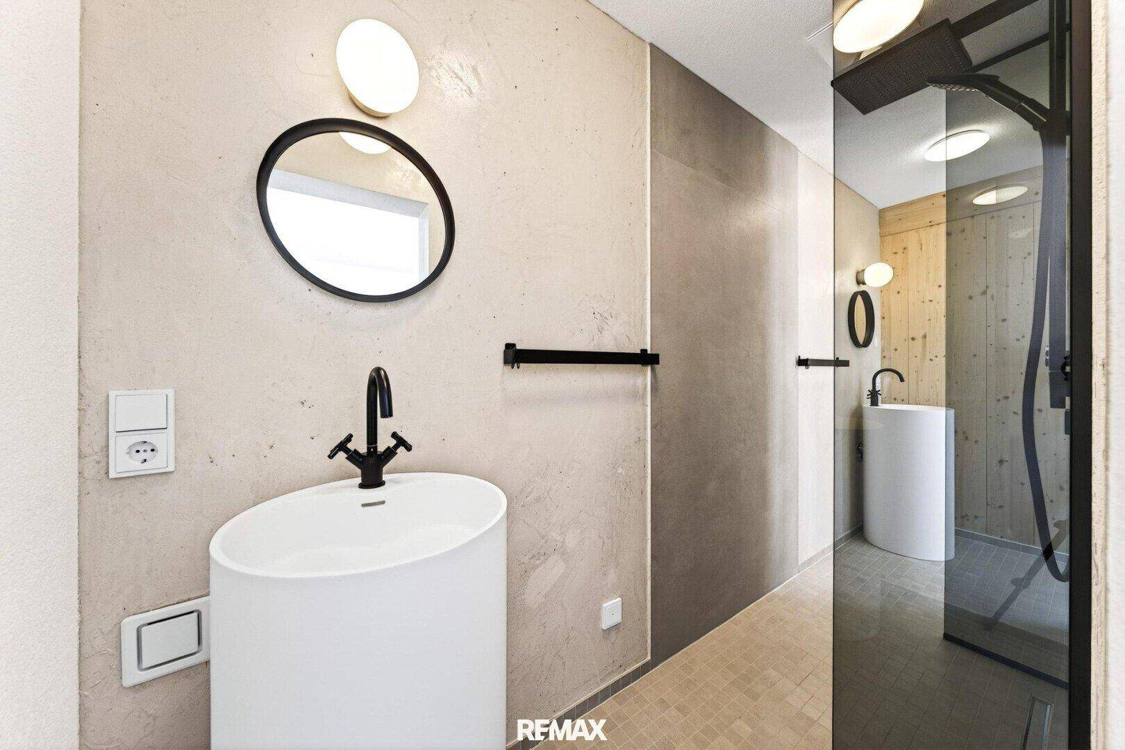 Elegantes Badezimmer mit modernem Waschbecken, runden Spiegeln und begehbarer Dusche.