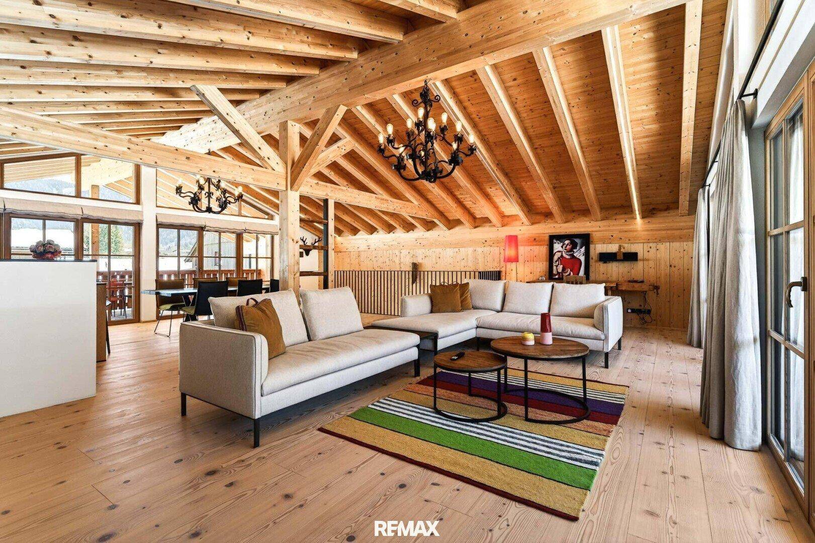 Gemütlicher Wohnbereich mit bequemen Sofas, Holzbalkendecke und farbenfrohem Teppich.