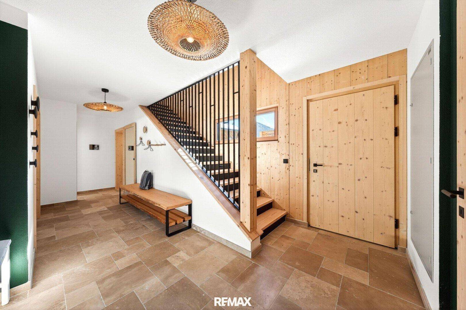 Heller Eingangsbereich mit Holzvertäfelung, Steinfliesenboden und einer modernen Treppe.