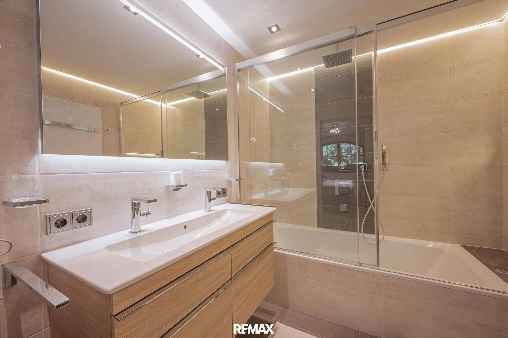 Modernes Badezimmer mit Doppelwaschbecken, Badewanne und integrierter Dusche hinter Glas.