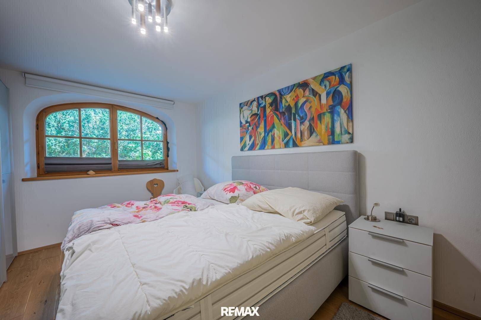 Helles Schlafzimmer mit Doppelbett, Holzboden und einem Fenster mit Rundbogen.