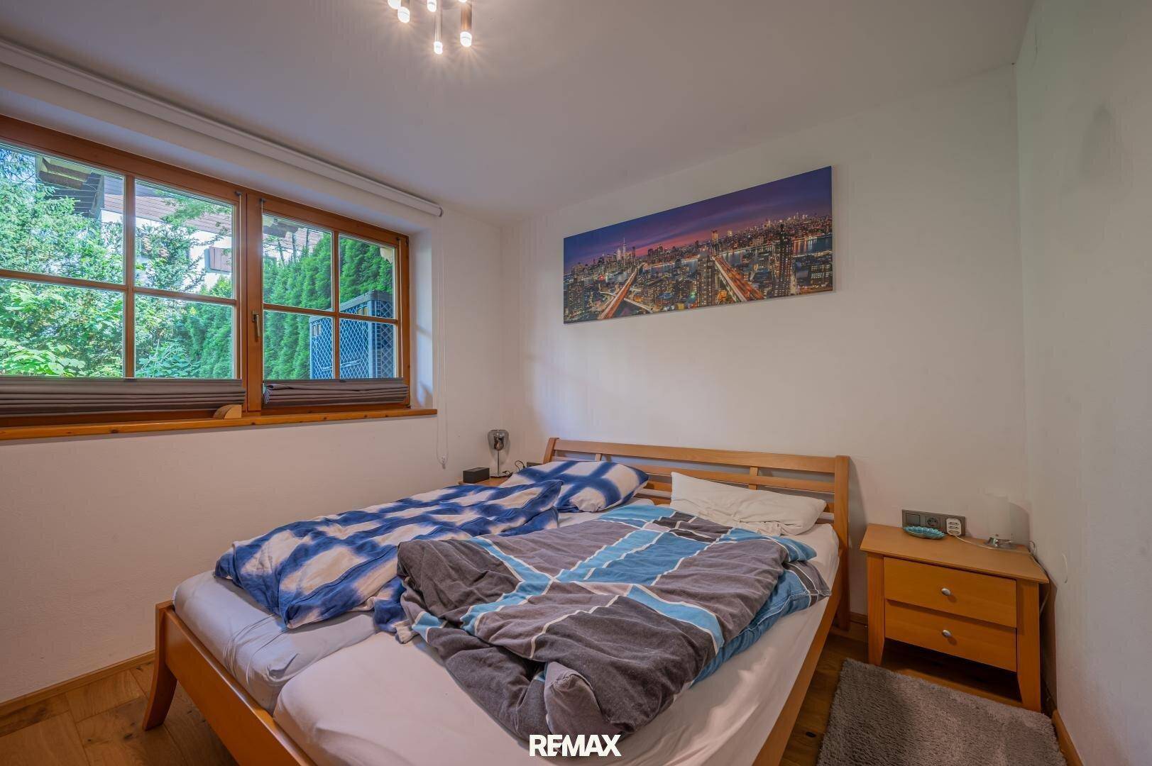 Schlafzimmer mit Doppelbett, Holzboden und Blick ins Grüne durch große Fenster.
