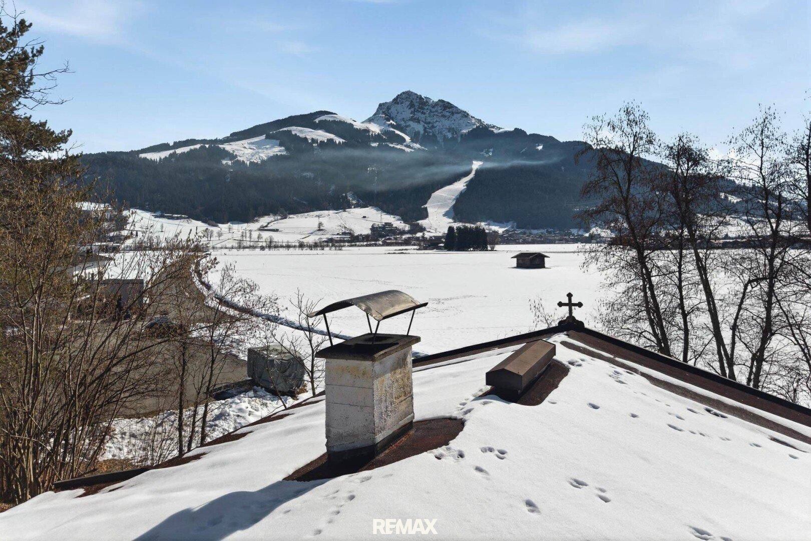 Panoramablick von einem verschneiten Dach über eine weite Winterlandschaft mit majestätischen Bergen im Hintergrund.