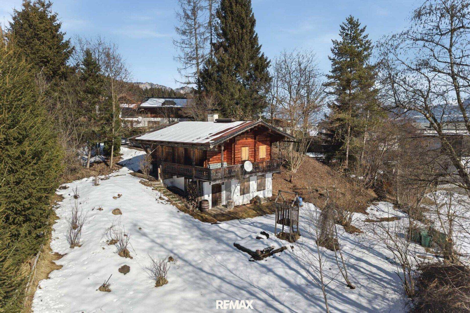 Nahaufnahme eines charmanten Holzhauses mit Balkon, umgeben von Schnee und Bäumen.