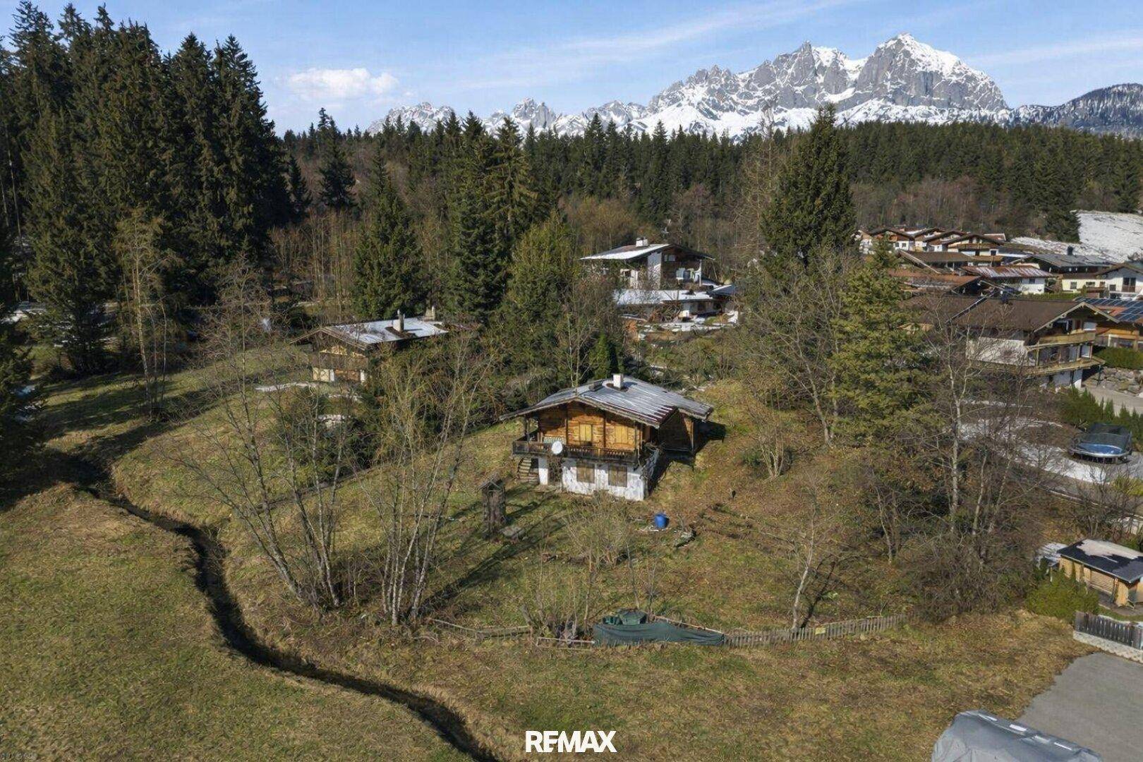 Luftaufnahme eines traditionellen Holzhauses in einer verschneiten Berglandschaft mit Wald.
