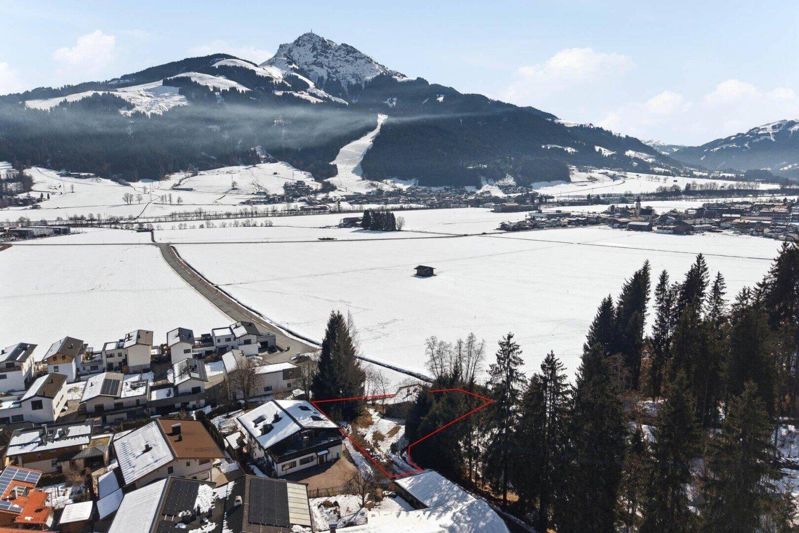 Weitläufige Winterlandschaft mit schneebedeckten Bergen und einem Dorf im Tal.
