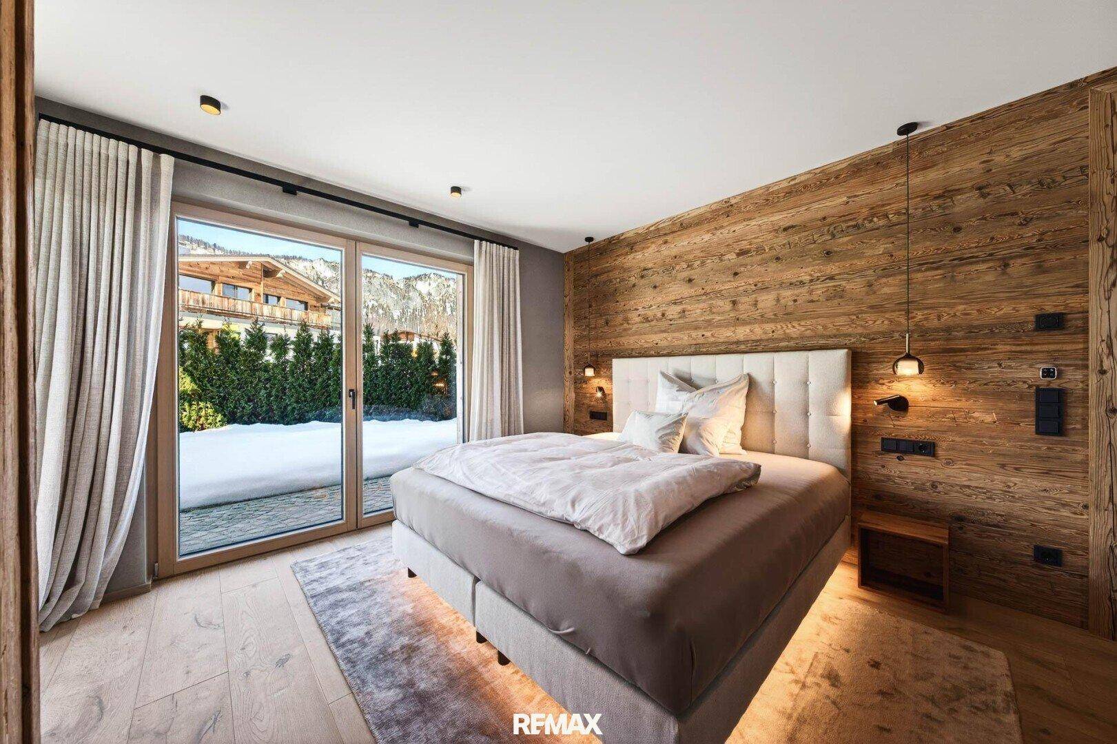 Helles Schlafzimmer mit Holzwand, großem Bett und direktem Zugang zu einem Außenbereich.