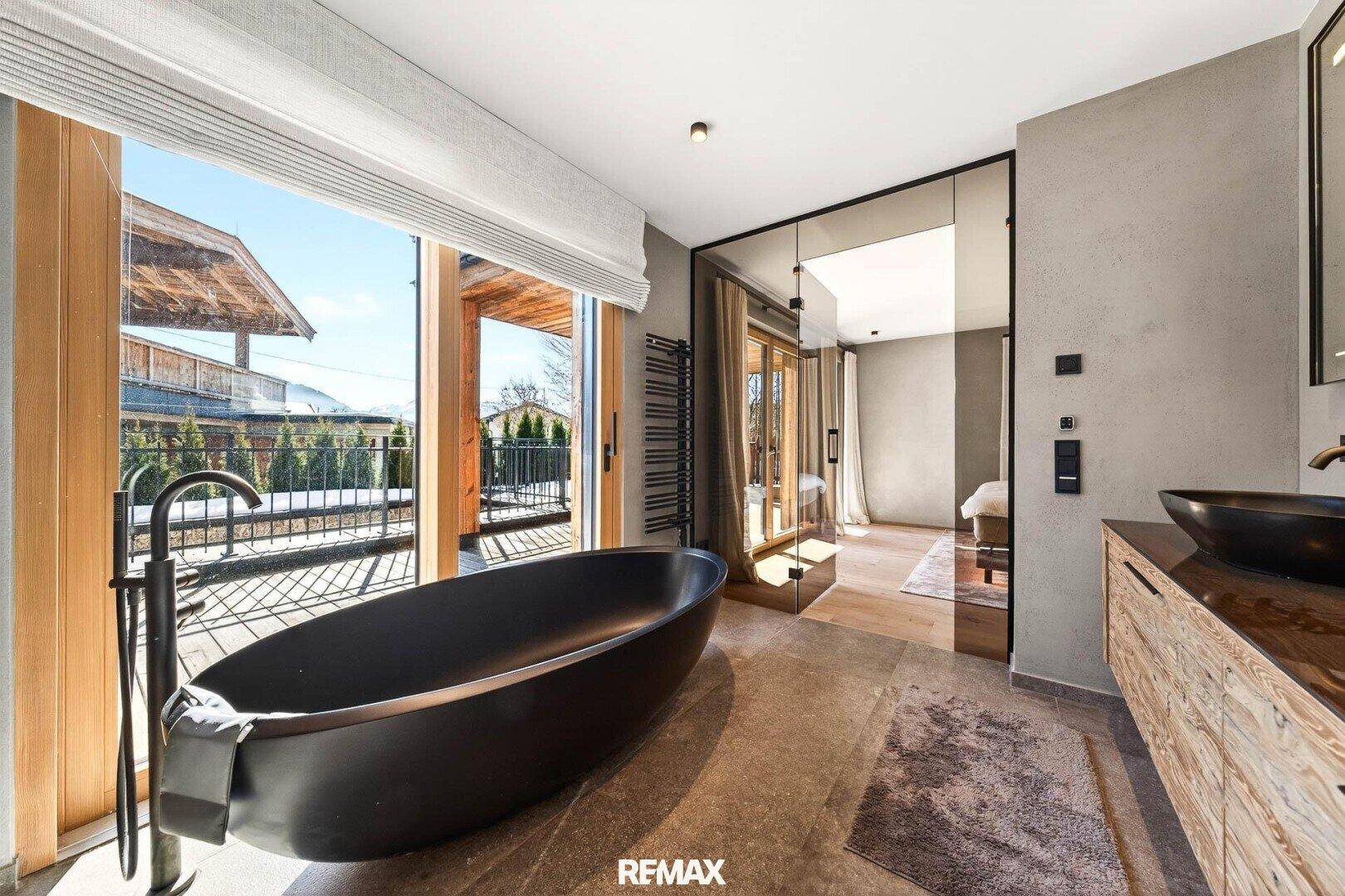 Luxuriöses Badezimmer mit freistehender schwarzer Badewanne und Panoramablick auf die Berge.