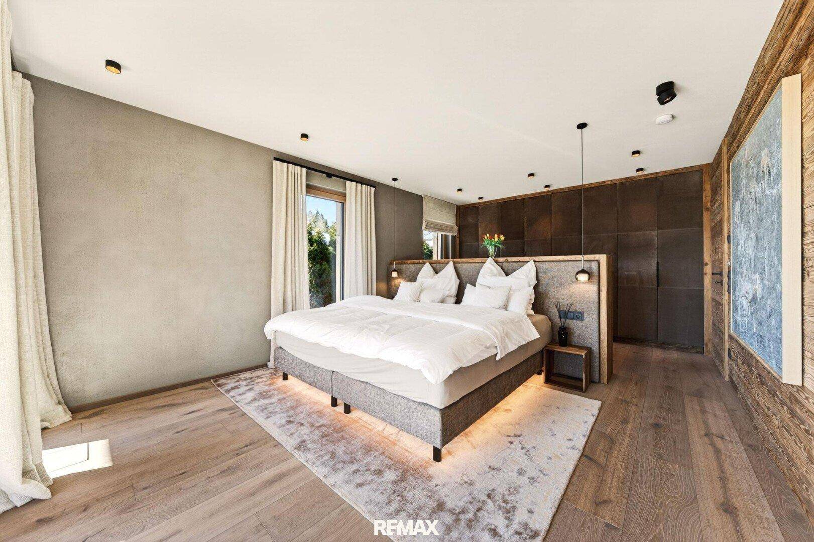 Modernes Schlafzimmer mit Holzwand, großem Bett und indirekter Beleuchtung für eine gemütliche Atmosphäre.
