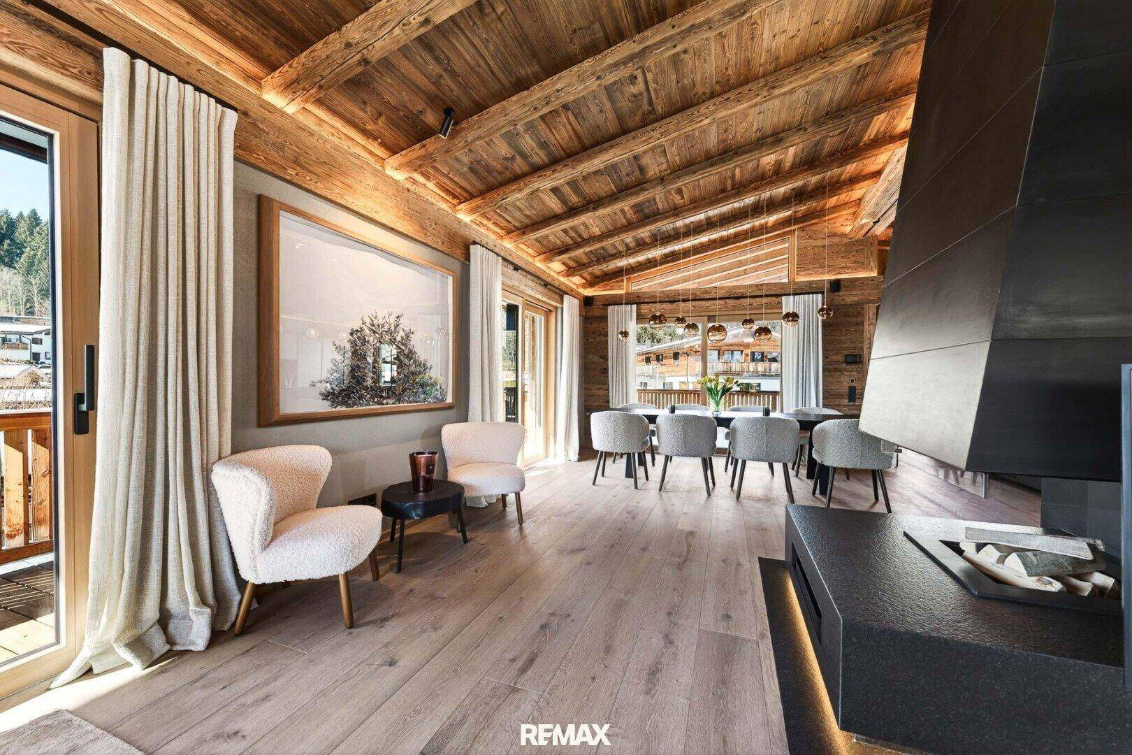 Offener Wohn- und Essbereich mit Holzbalkendecke, Kamin und Zugang zu einem Balkon.