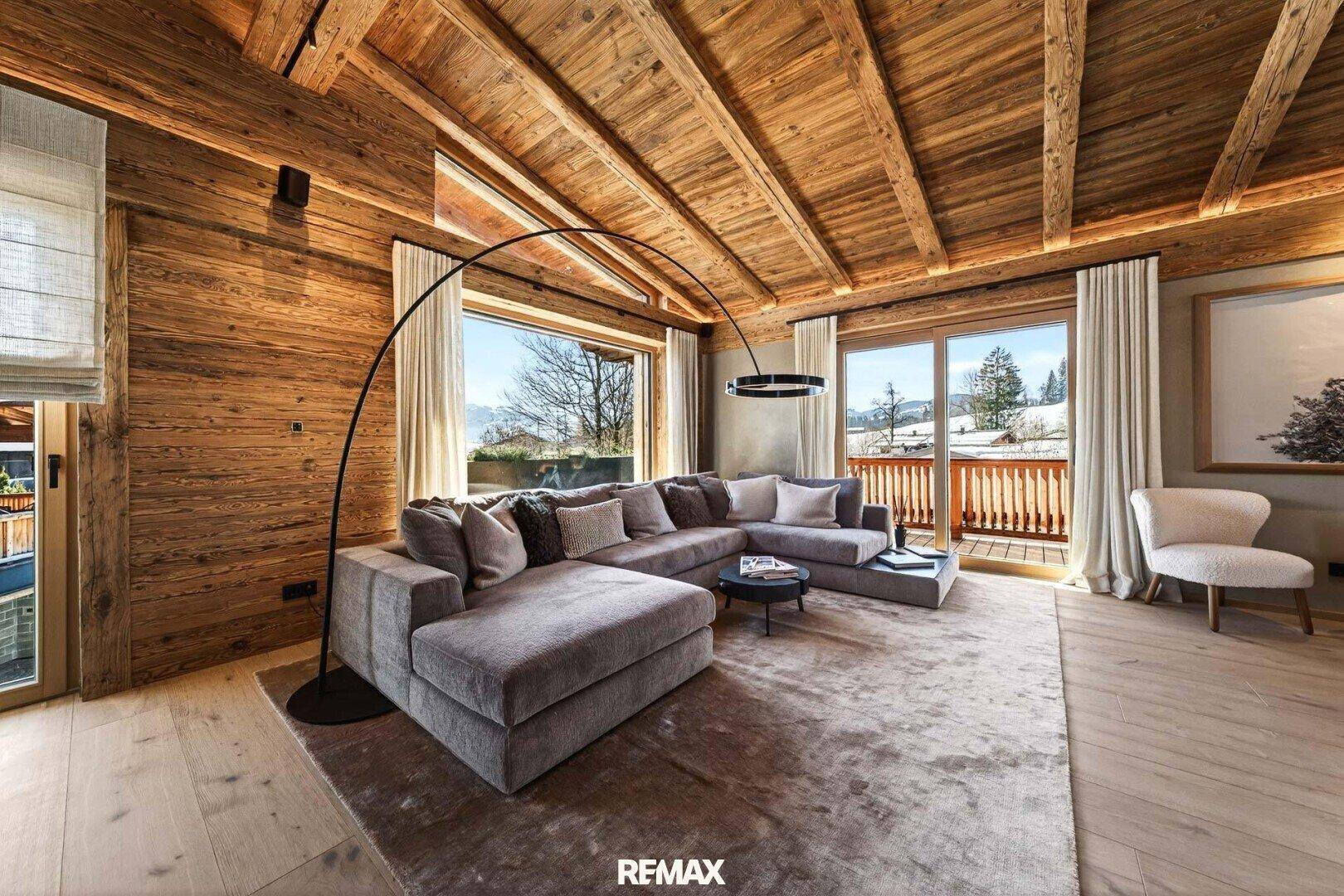 Gemütliches Wohnzimmer im alpinen Stil mit großem Ecksofa, Holzwänden und Zugang zum Balkon.