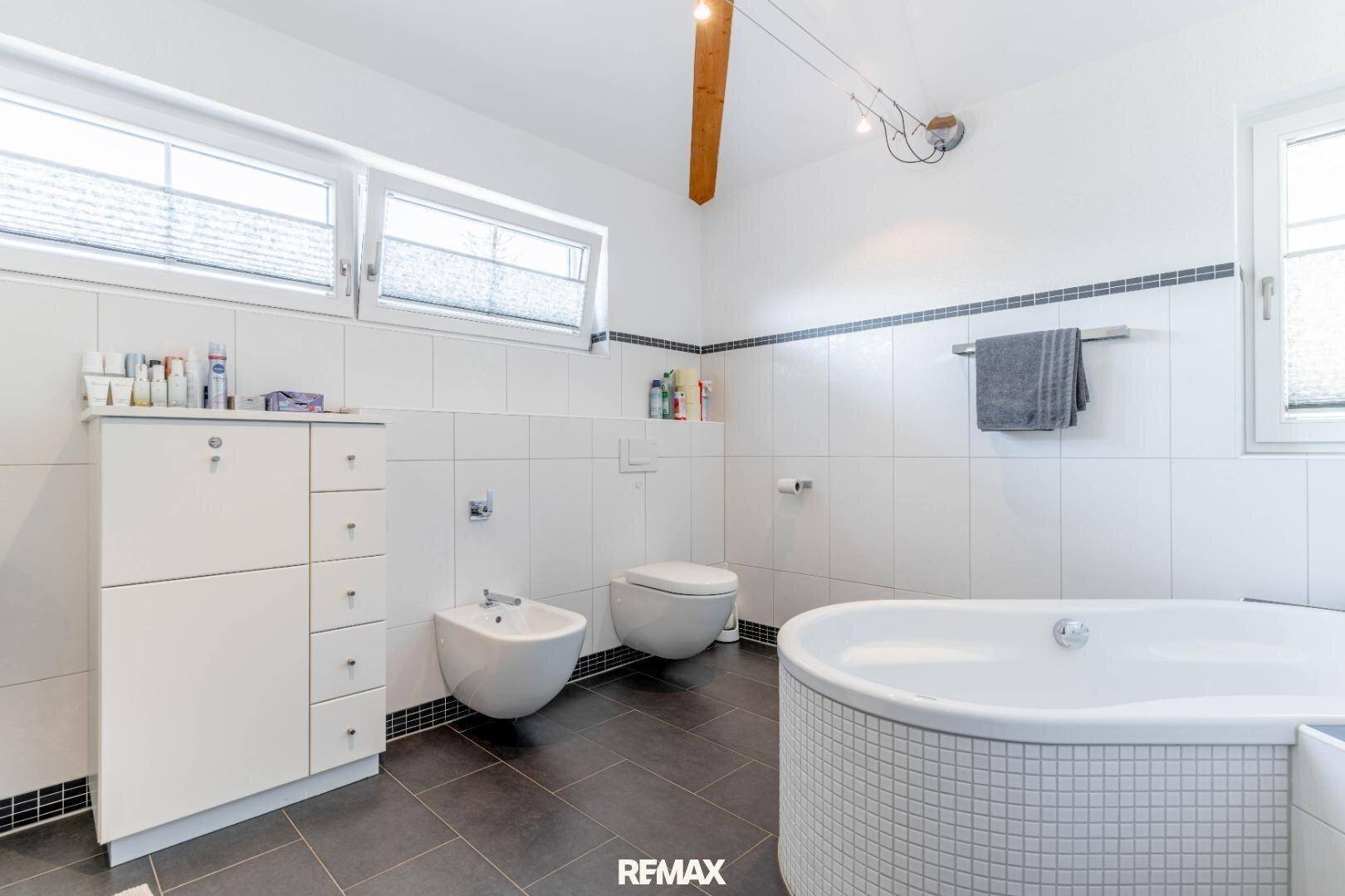 Modernes Badezimmer mit runder Badewanne, Bidet, Wand-WC und Fenster für natürliche Belüftung.
