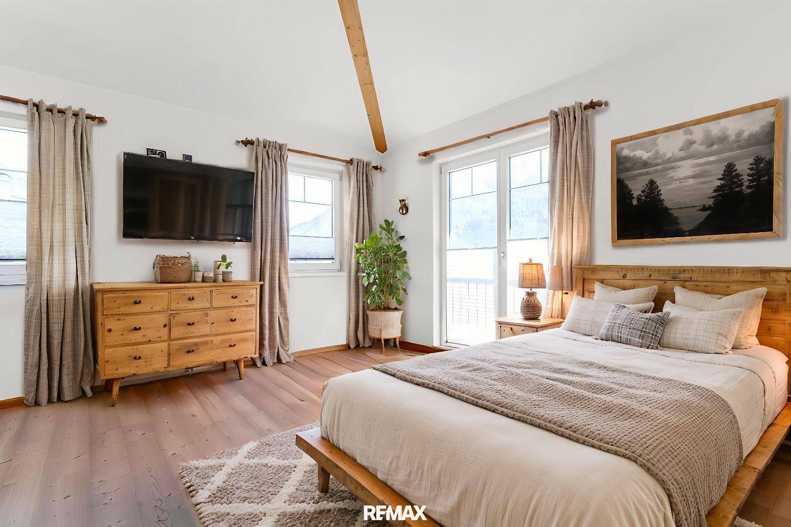 Gemütliches Schlafzimmer mit Holzboden, sichtbarem Deckenbalken und Zugang zu einem Balkon.