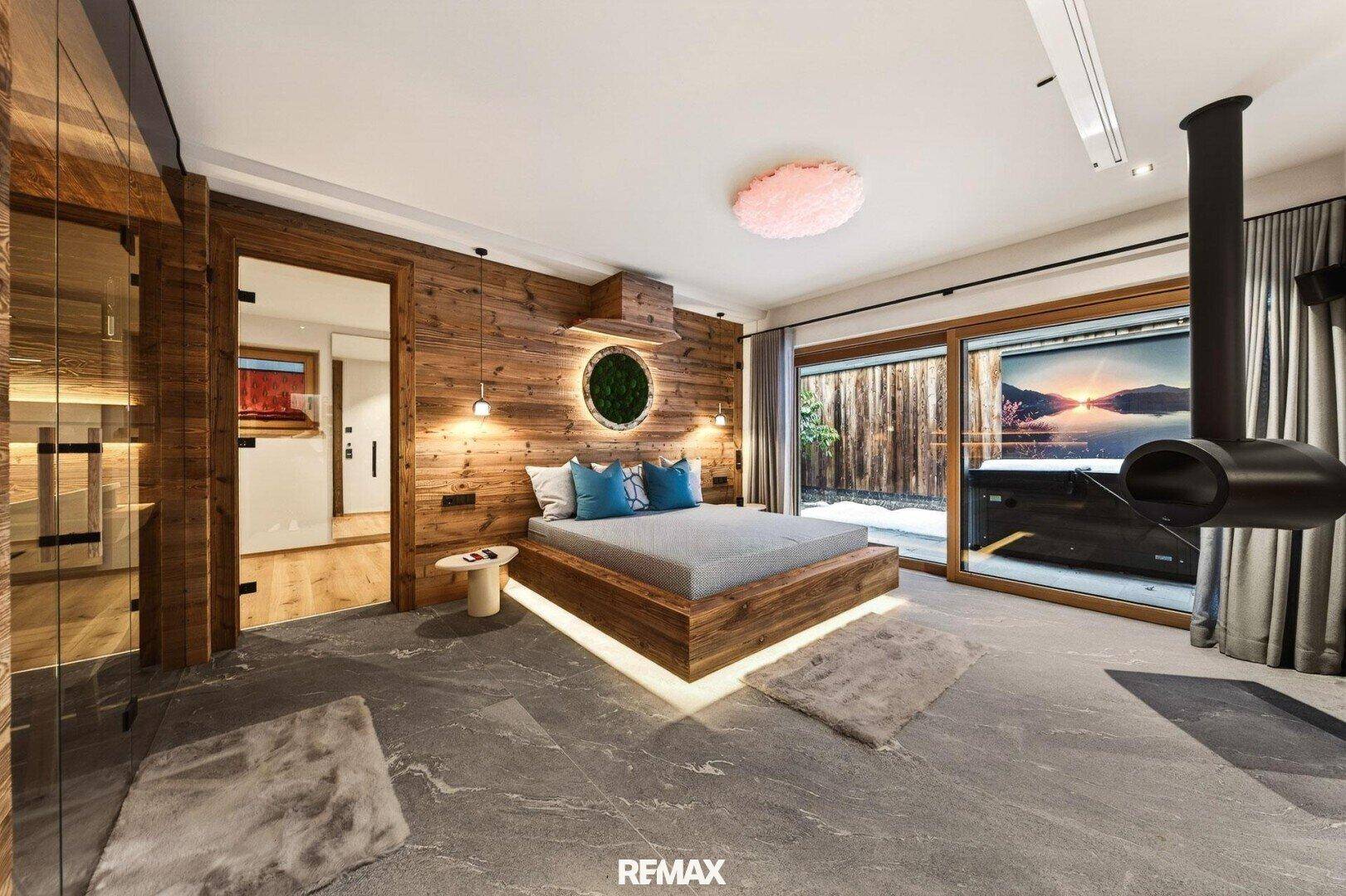 Exklusives Schlafzimmer mit Holzwand, Steinfliesen und einem modernen Hängekamin.