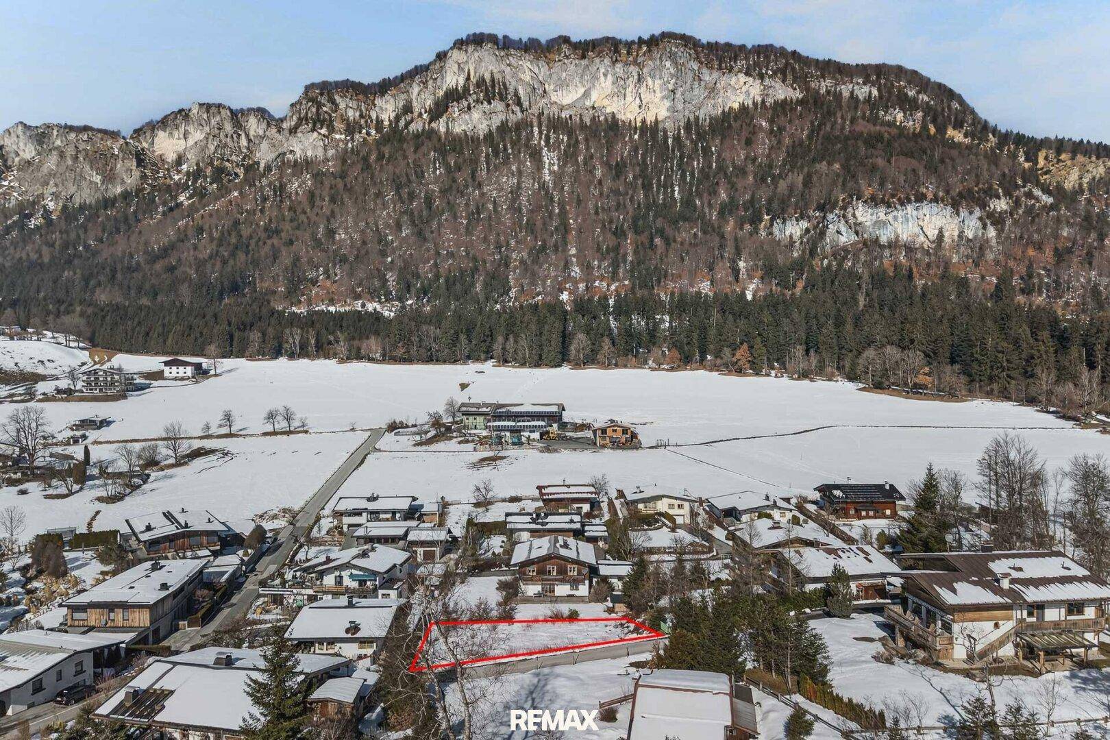 Luftaufnahme eines Grundstücks in einer verschneiten Berglandschaft mit umliegenden Häusern und Wald.