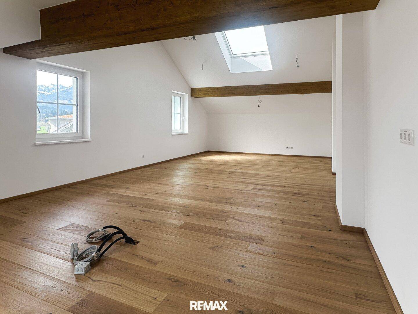 Heller, leerer Raum im Dachgeschoss mit Holzbalken, Holzboden und Dachfenster.