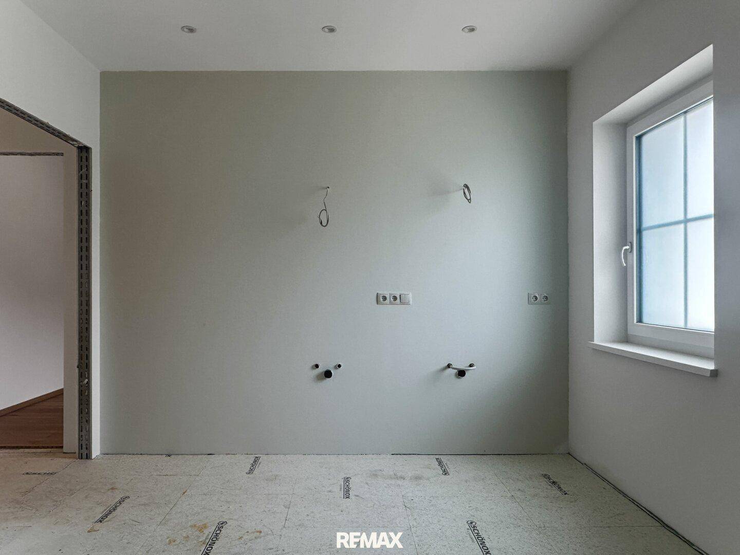 Unfertiger Raum mit sichtbaren Sanitäranschlüssen und einem Fenster, bereit für den Ausbau.