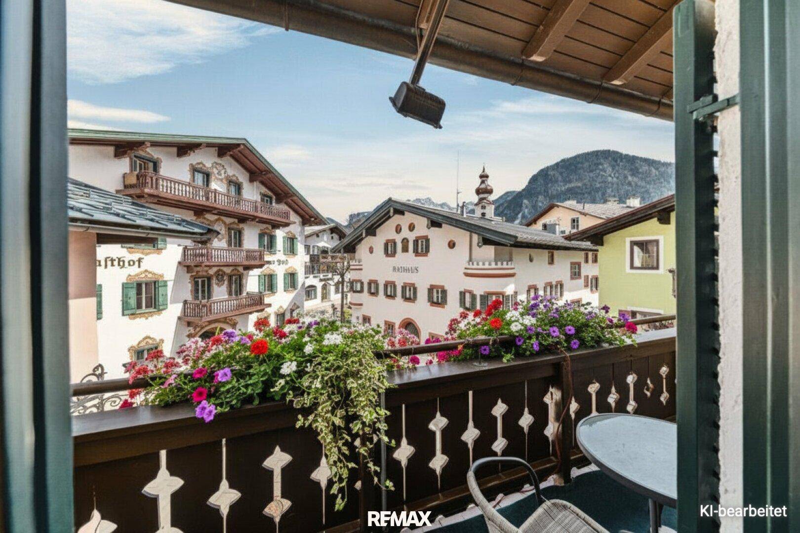 Gemütlicher Balkon mit bunten Blumenkästen und malerischem Blick auf die umliegenden Alpenhäuser und Berge.
