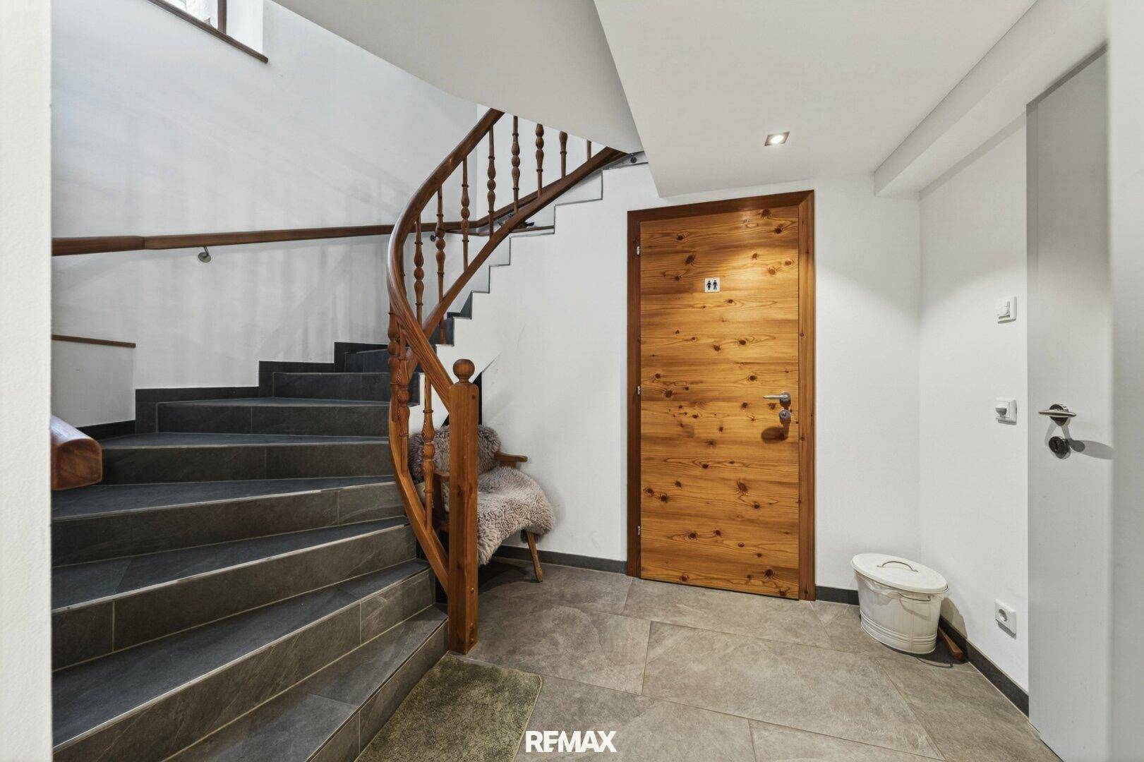 Elegante Holztreppe mit geschwungenem Geländer und Fliesenboden in einem hellen Eingangsbereich.