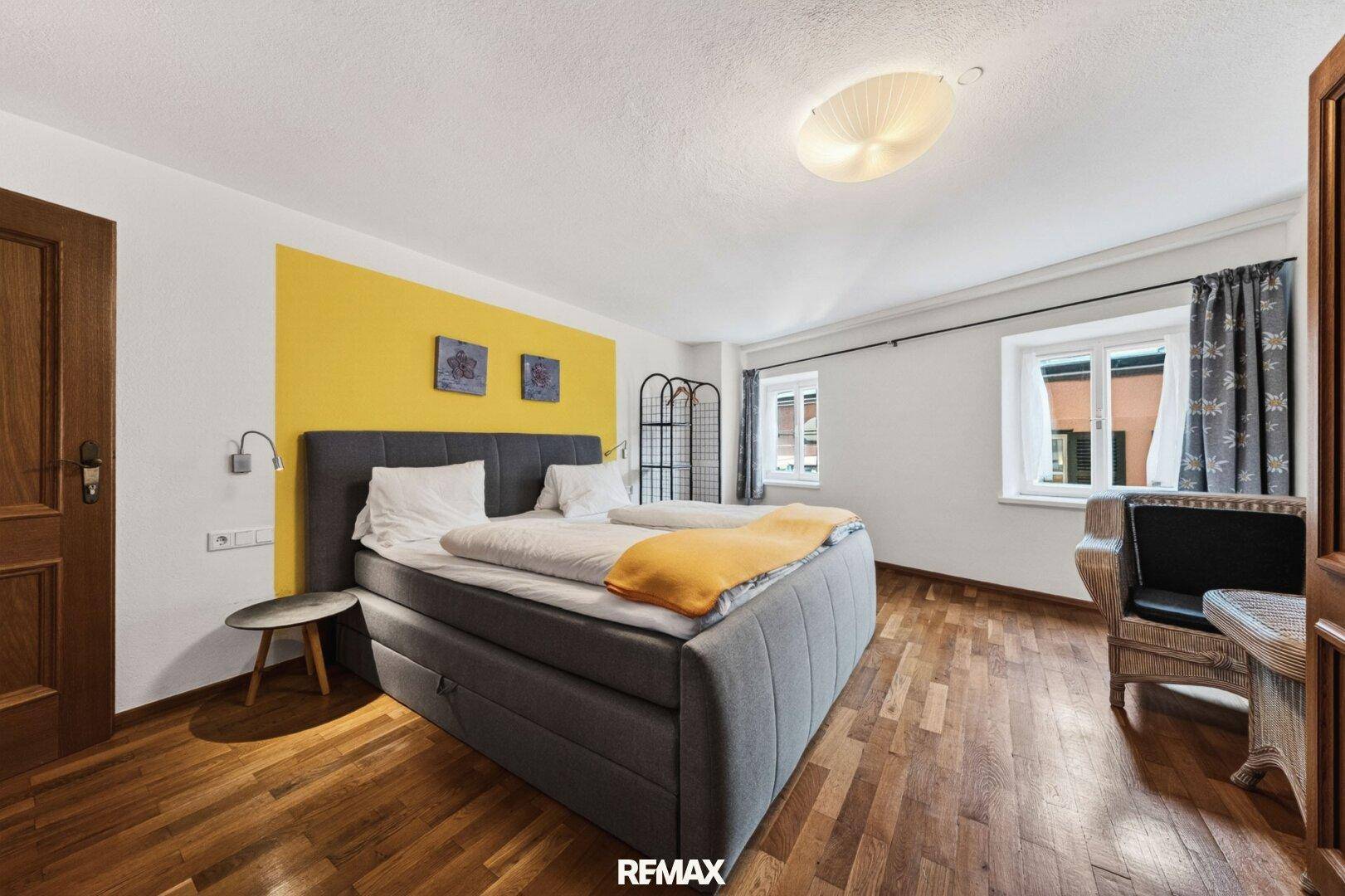 Helles Schlafzimmer mit modernem Boxspringbett, Holzboden und gelber Akzentwand.