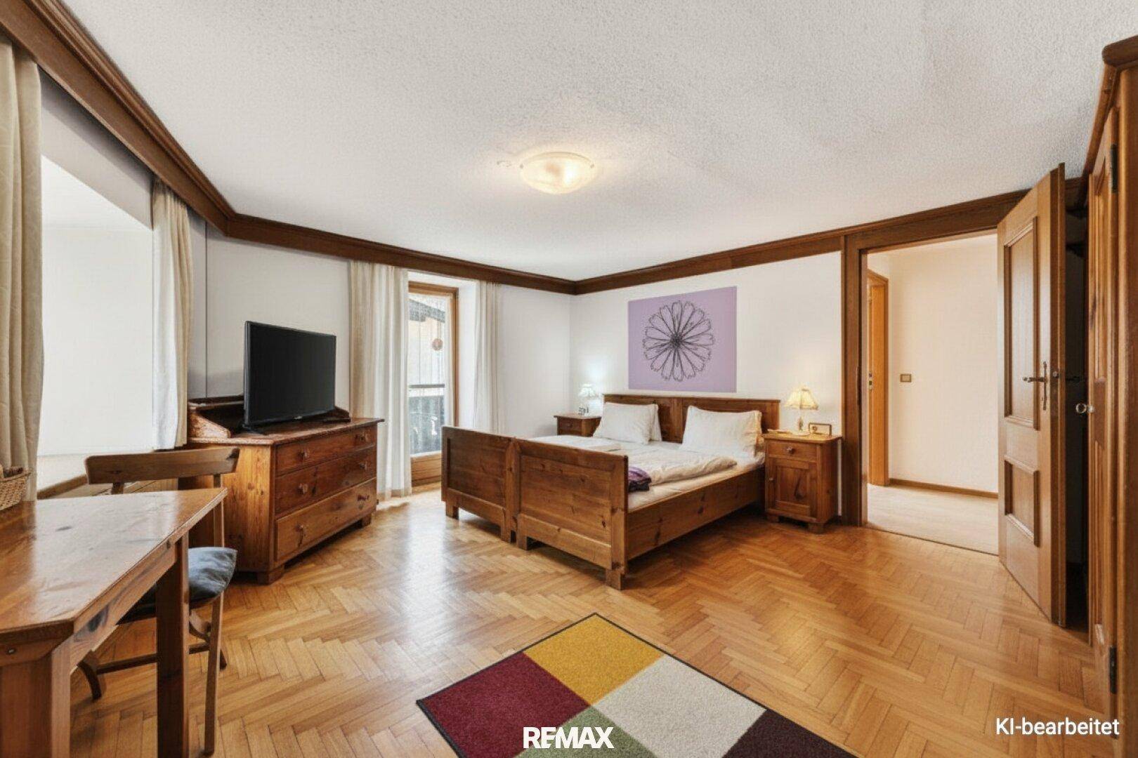 Gemütliches Schlafzimmer mit traditionellen Holzmöbeln, Parkettboden und Zugang zu einem weiteren Raum.