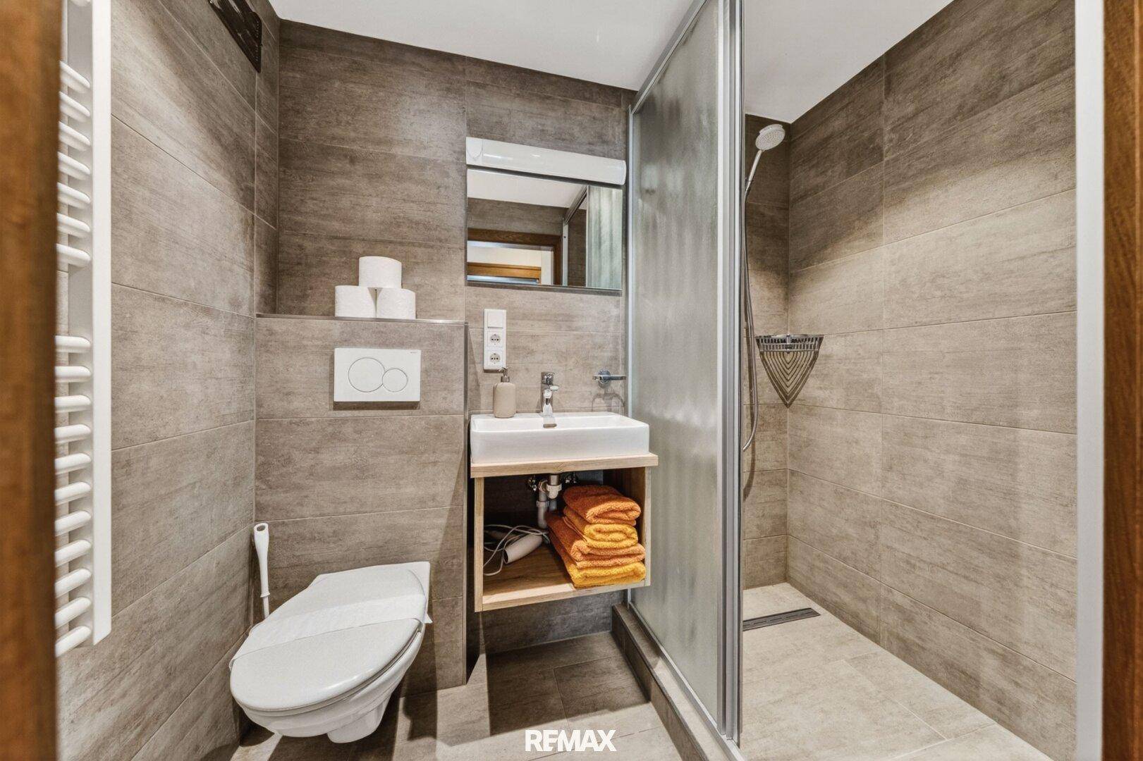 Modernes Badezimmer mit begehbarer Dusche, Wand-WC und eleganten grauen Fliesen.