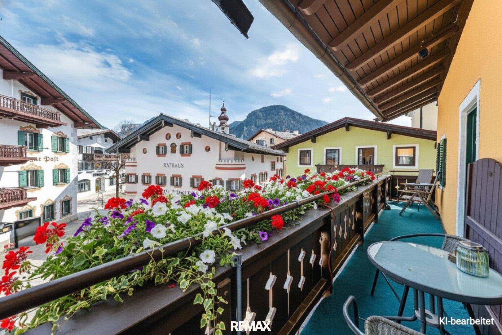 Balkon mit bunten Blumenkästen, Sitzgelegenheiten und Blick auf die umliegenden Gebäude und Berge.