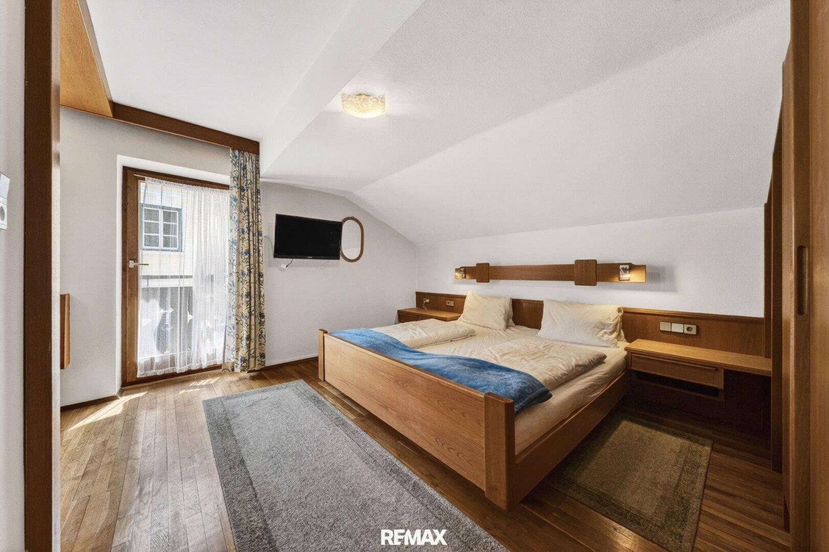 Gemütliches Schlafzimmer mit Holzbett, Holzboden und Zugang zu einem französischen Balkon.