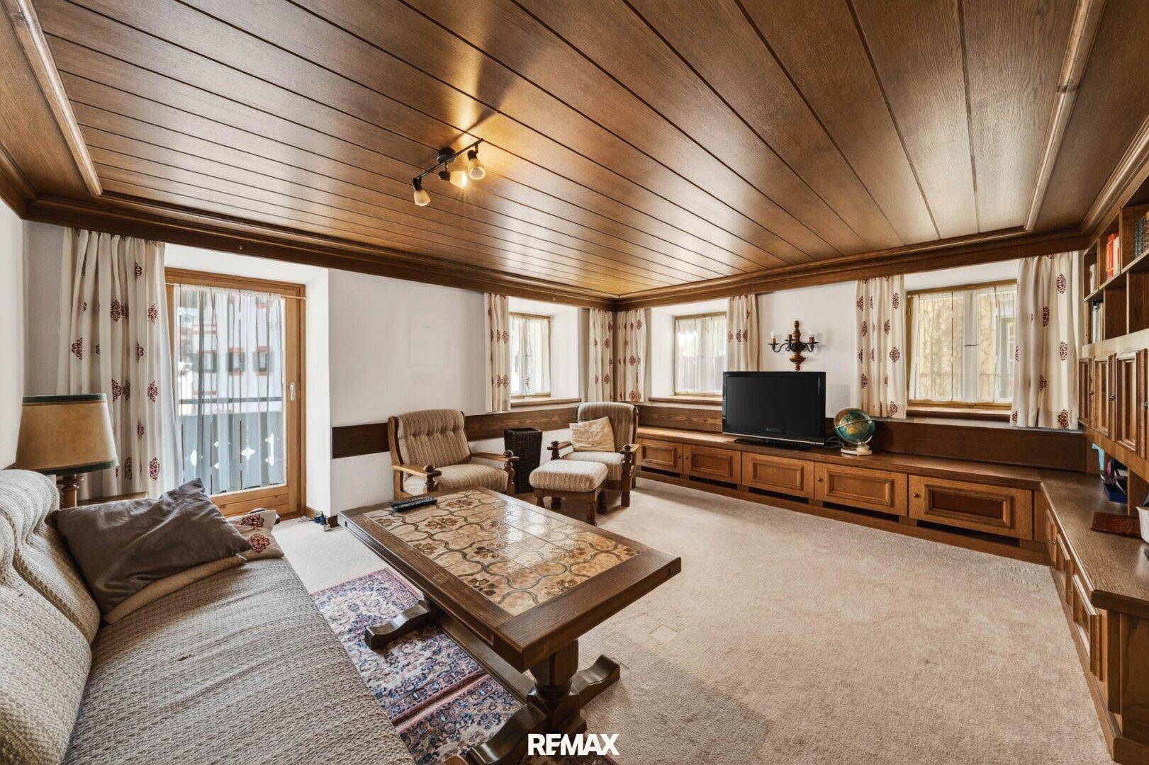 Gemütliches Wohnzimmer im alpinen Stil mit Holzvertäfelung, Teppichboden und traditionellen Möbeln.