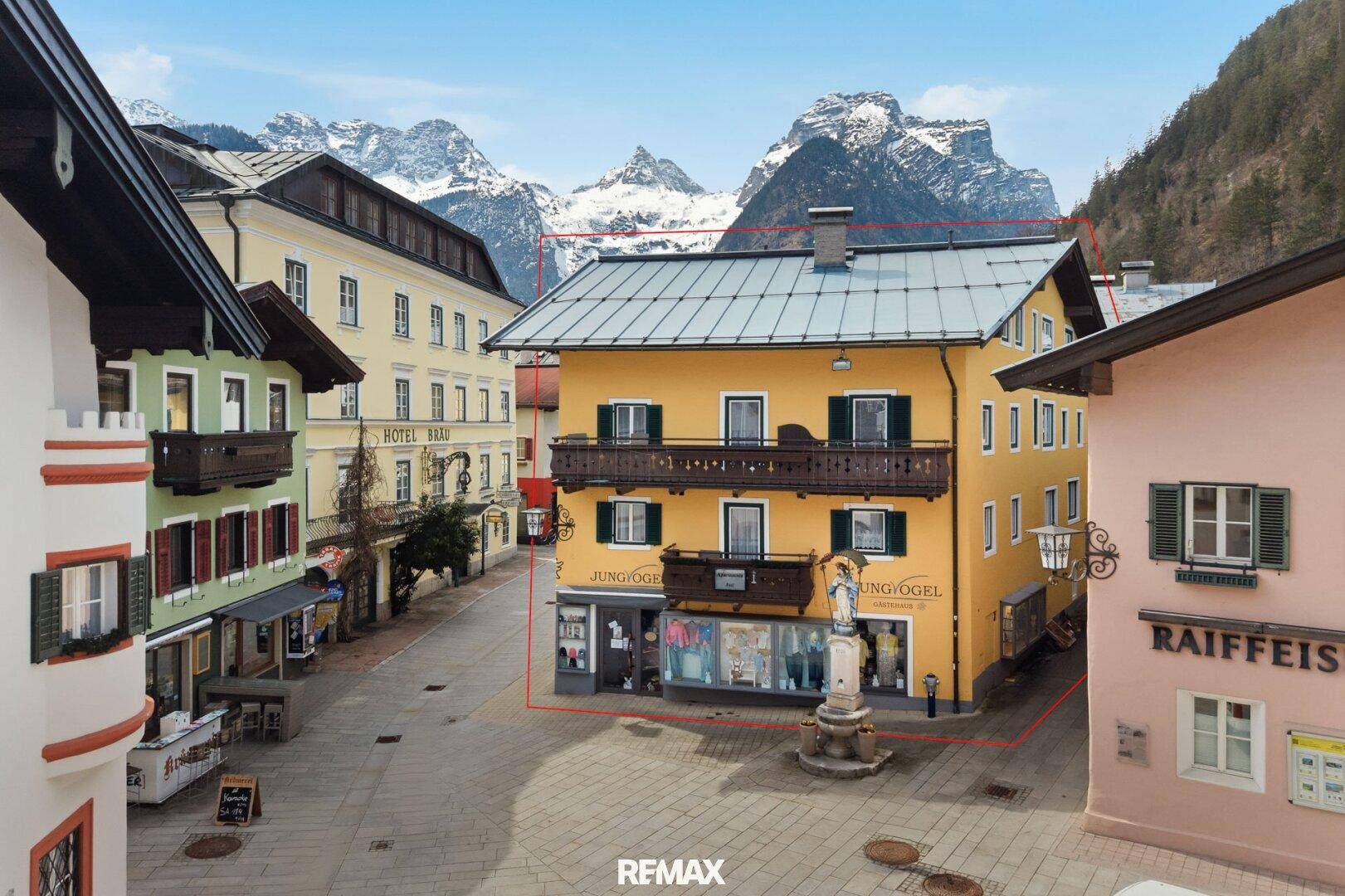 Traditionelles Gebäude in einer Bergstadt mit Geschäften im Erdgeschoss und schneebedeckten Bergen im Hintergrund.