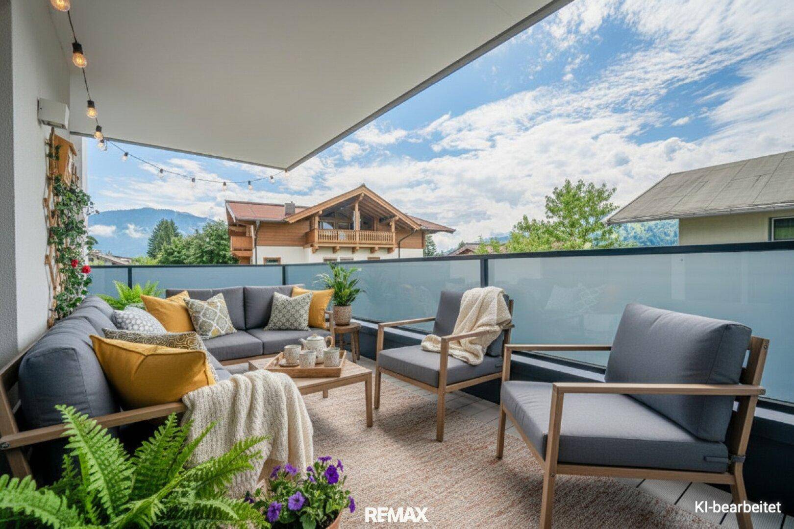 Großer Balkon mit bequemen Loungemöbeln und Blick auf die umliegende Berglandschaft unter blauem Himmel.