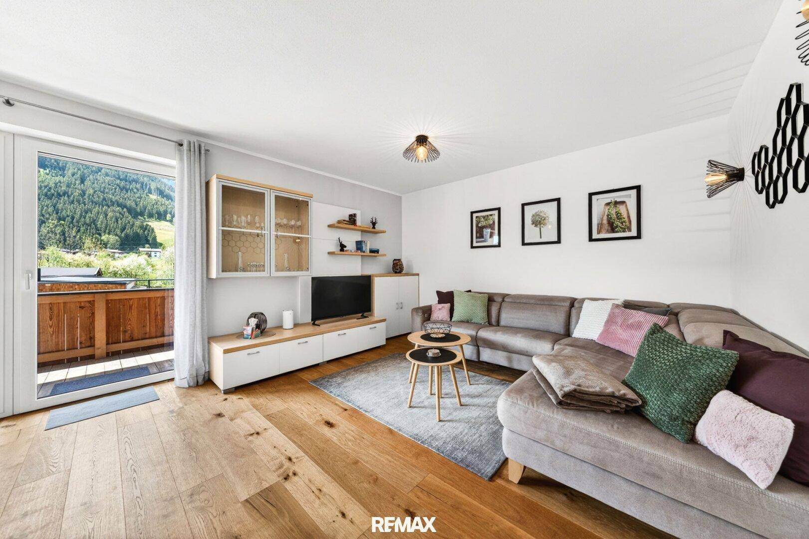 Helles Wohnzimmer mit großem Sofa, Holzboden und Zugang zum Balkon mit Bergblick.