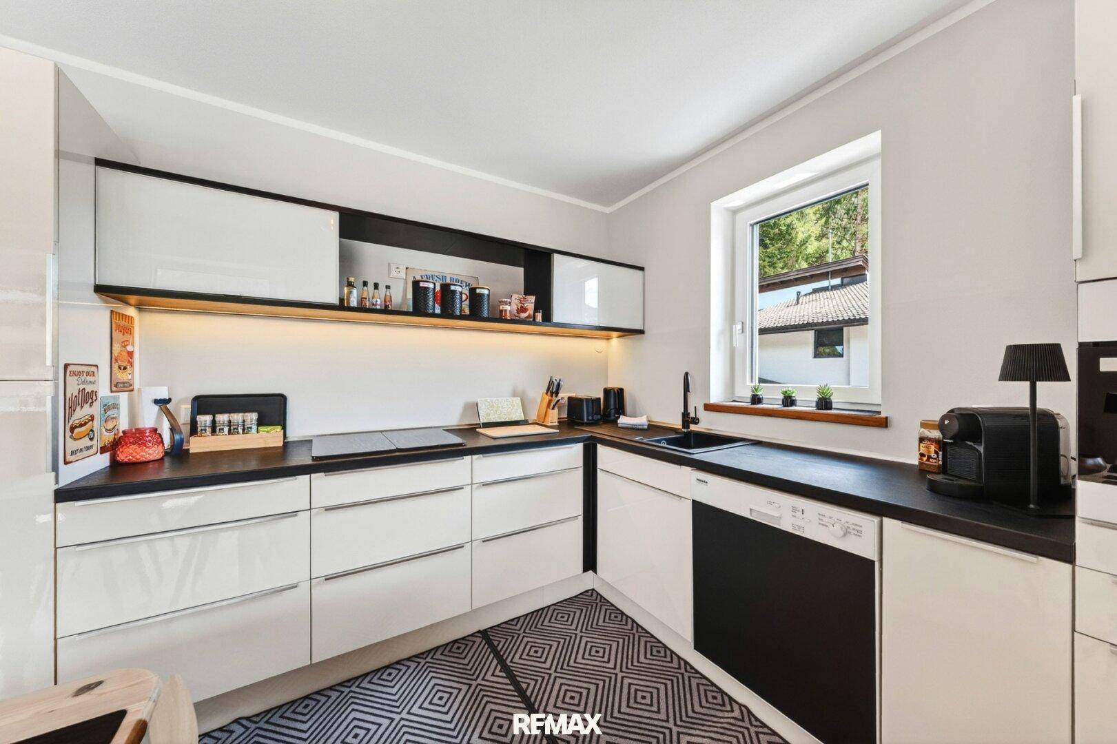 Moderne Küche mit weißen Hochglanzfronten, schwarzen Arbeitsplatten und Fenster.
