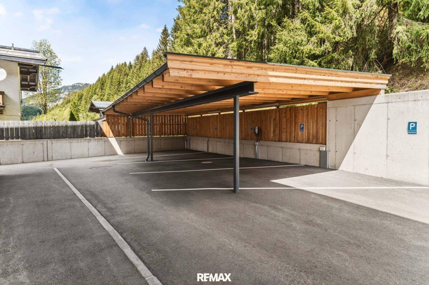 Überdachter Carport mit Holzkonstruktion und Ladestation für Elektrofahrzeuge.