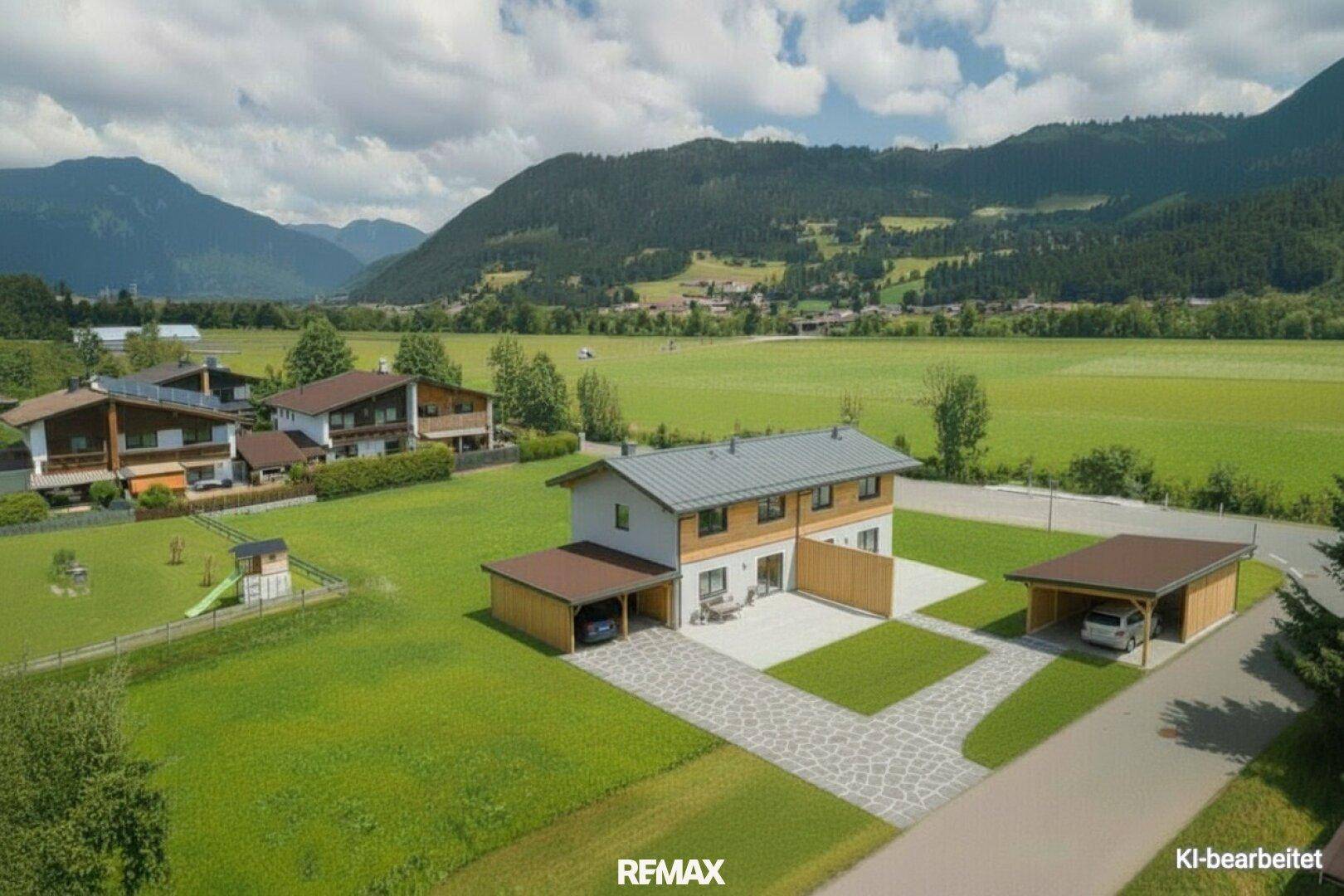 Luftaufnahme eines modernen Hauses mit Garten, Carports und Spielplatz vor alpiner Bergkulisse.