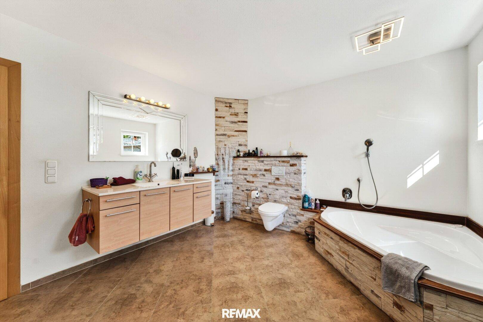 Geräumiges Badezimmer mit Badewanne, Doppelwaschbecken und modernen Fliesen an Wänden und Boden.