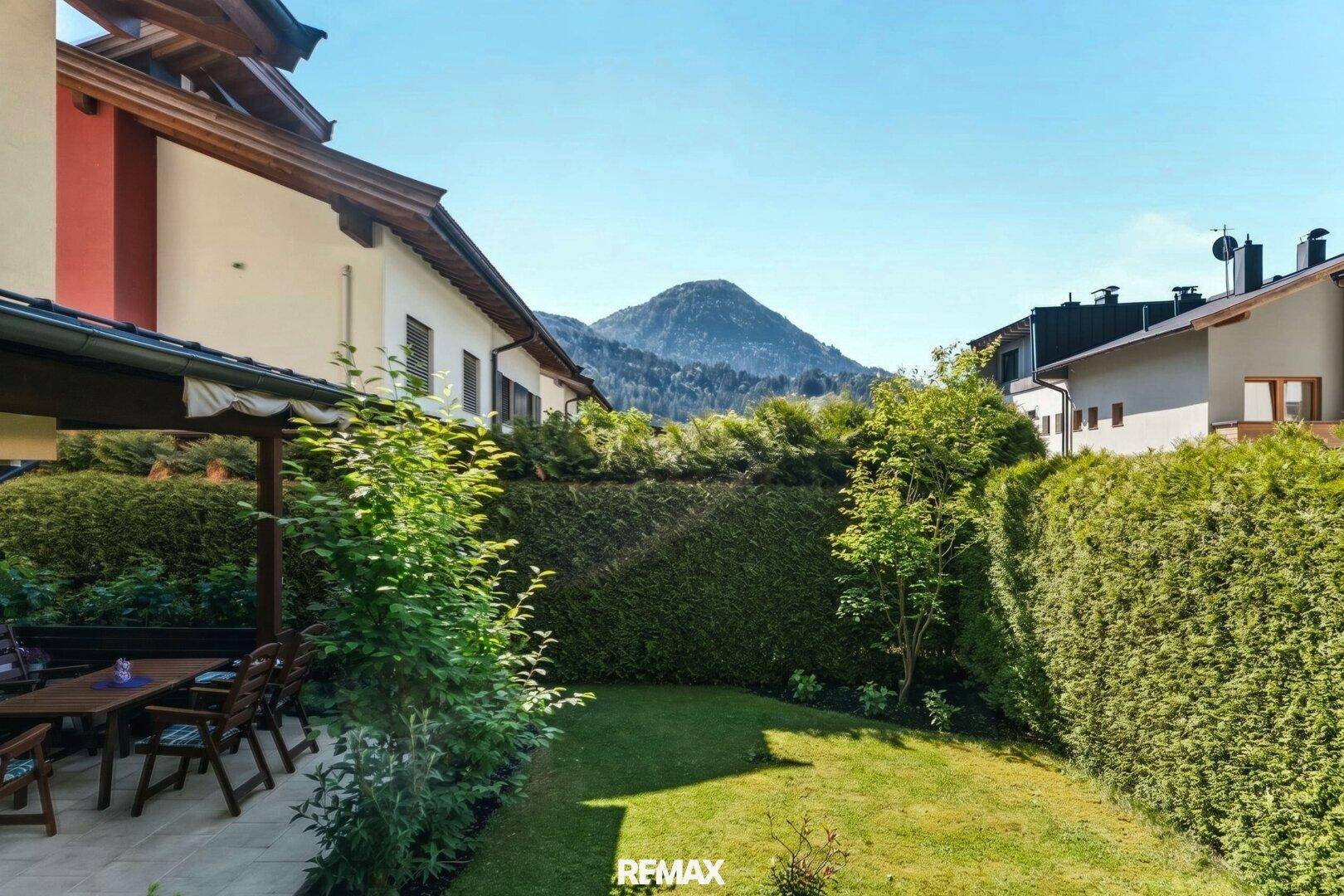 Gepflegter Gartenbereich mit Rasenfläche, Hecke und beeindruckendem Bergblick im Hintergrund.