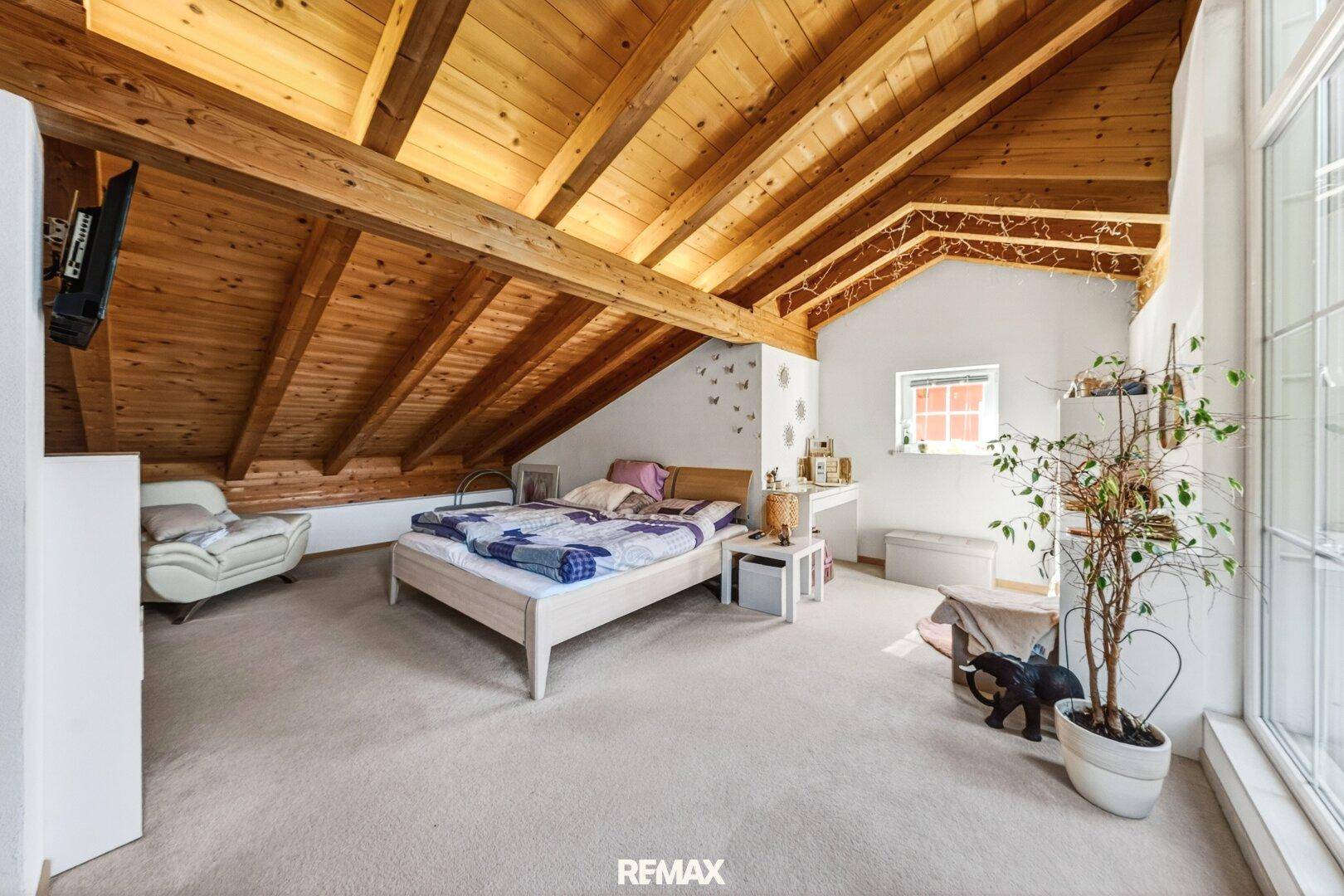 Gemütliches Dachgeschoss-Schlafzimmer mit Holzbalken und Teppichboden.