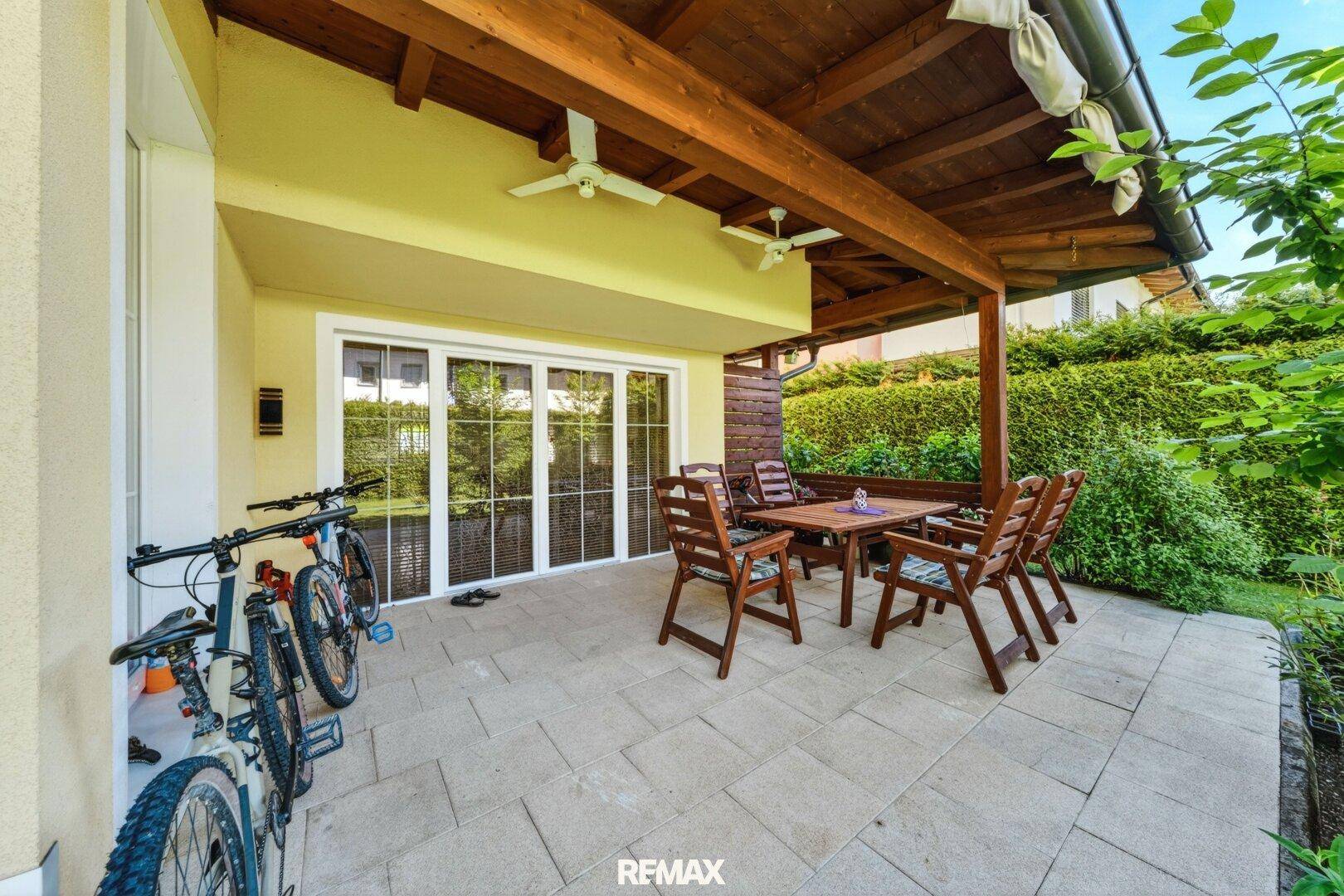 Überdachte Terrasse mit Steinplattenboden und Holzmöbeln für entspannte Stunden im Freien.